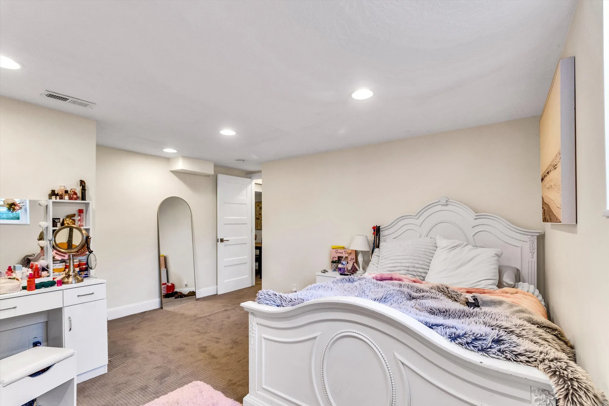 Recessed ceiling lighting illuminates a carpeted bedroom with light neutral wall tones