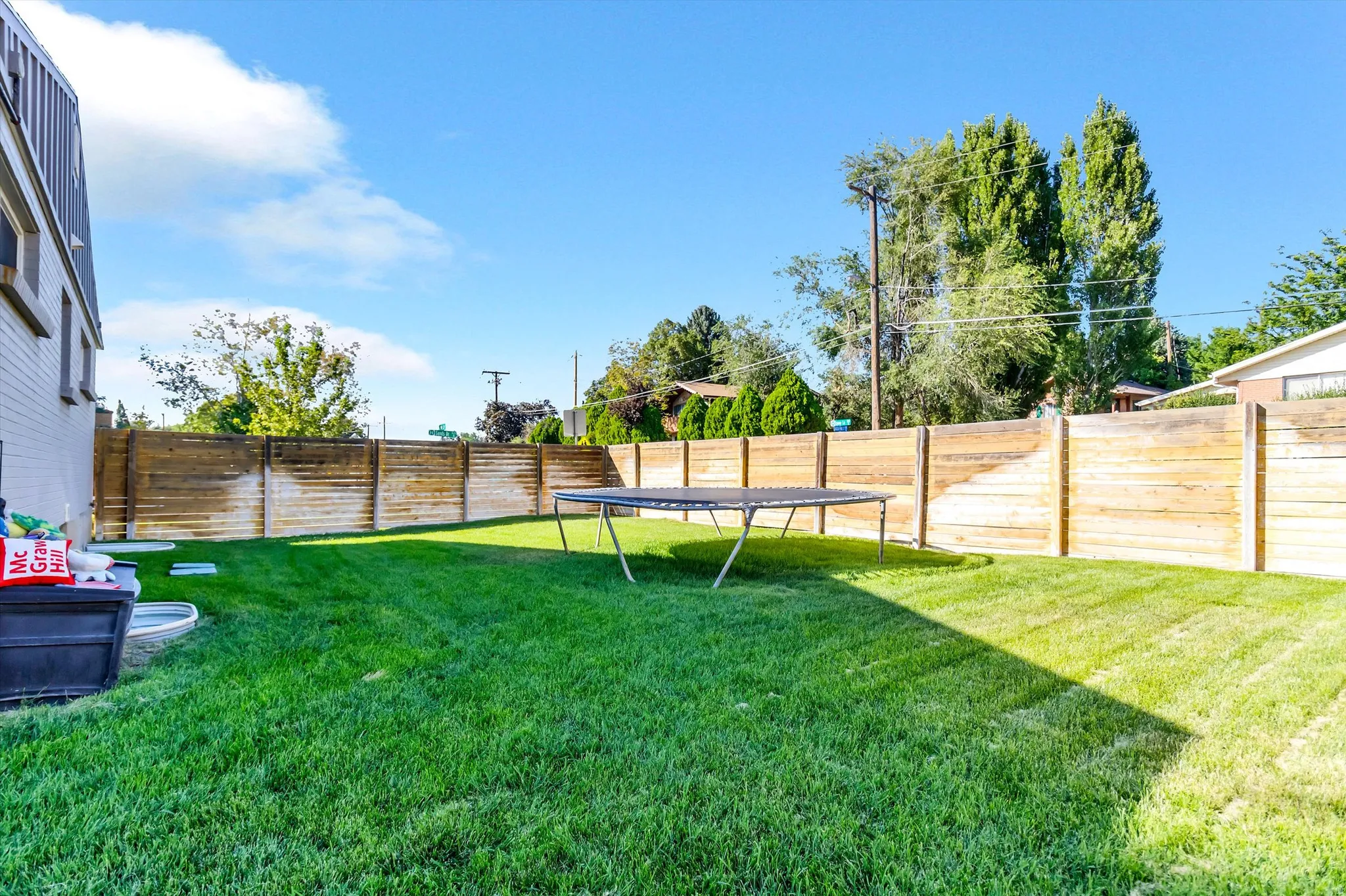 Spacious backyard featuring a manicured lawn, a full-height wooden fence, and mature perimeter trees