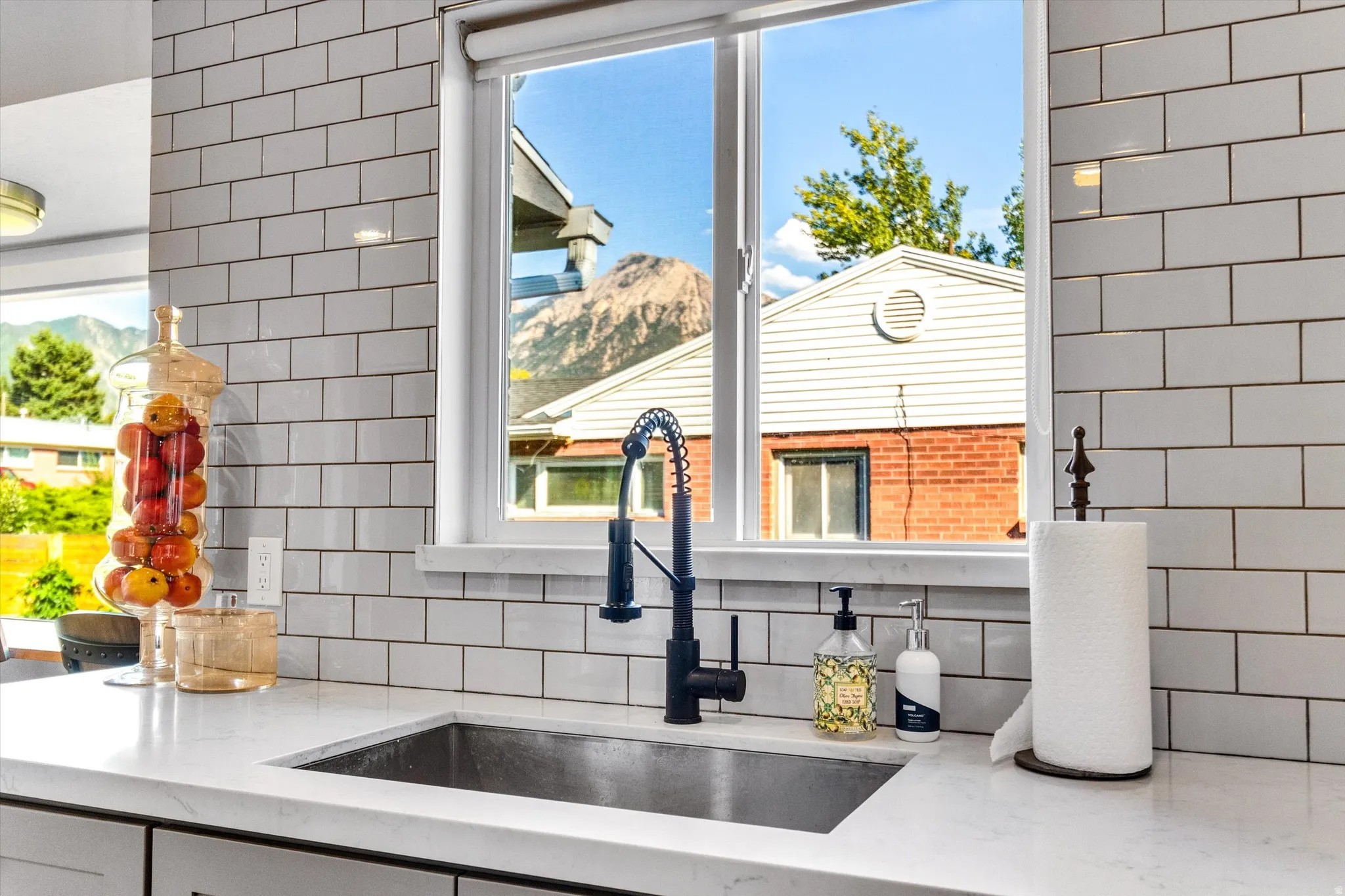 Kitchen sink area featuring white subway tile backsplash, white countertops, a single-basin sink, and a black gooseneck faucet