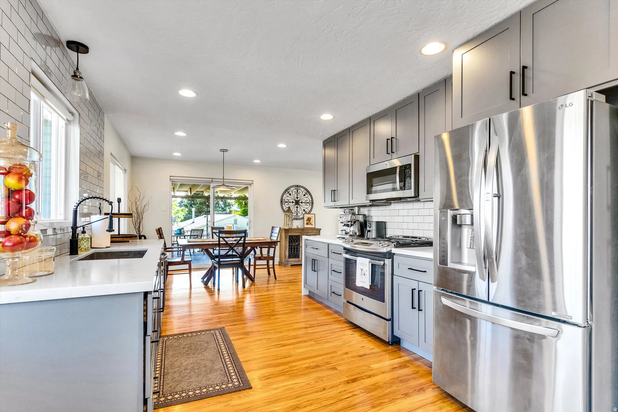 Kitchen featuring grey cabinetry with matte black hardware, stainless steel appliances, subway tile backsplash, and light wood-finish flooring