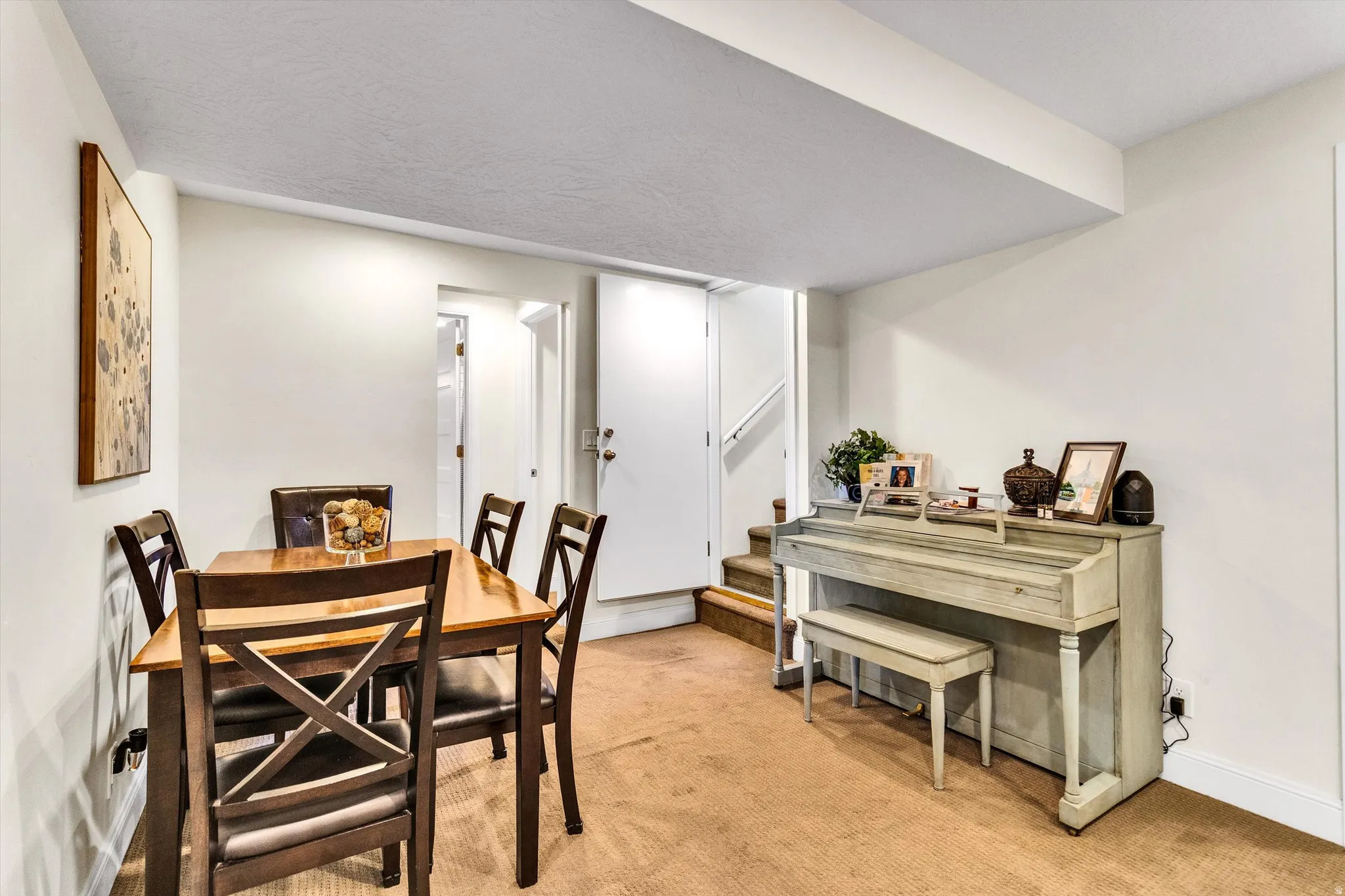Carpeted room featuring a dining area with a wooden table and chairs, white painted walls, a built-in staircase, and a doorway