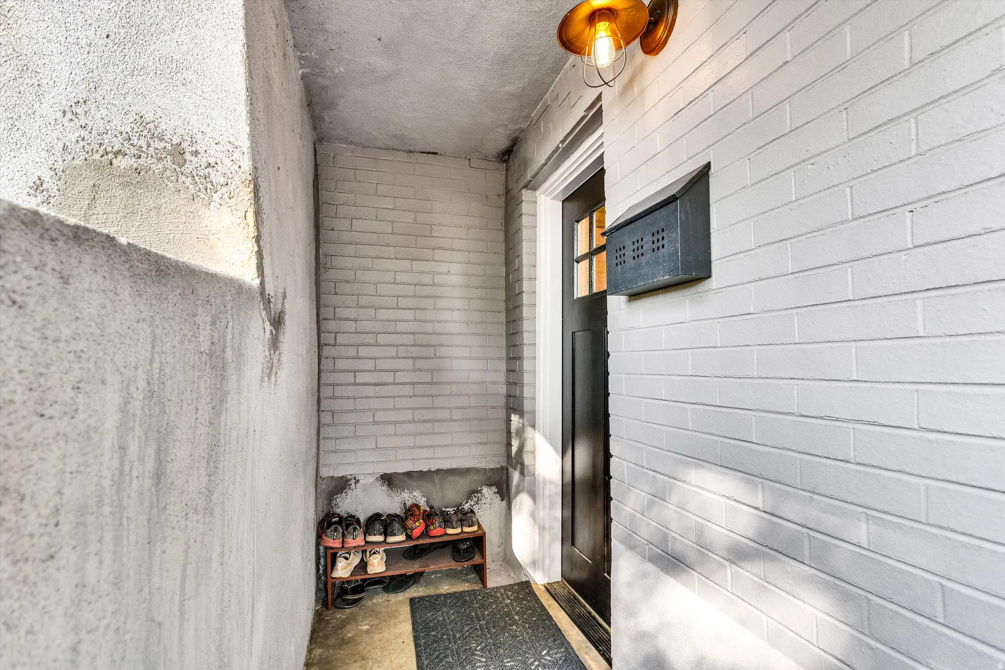 Entryway featuring white painted brick, a black door with window panes, and an industrial-style overhead light fixture