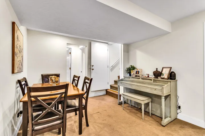 Carpeted room featuring a dining area with a wooden table and chairs, white painted walls, a built-in staircase, and a doorway