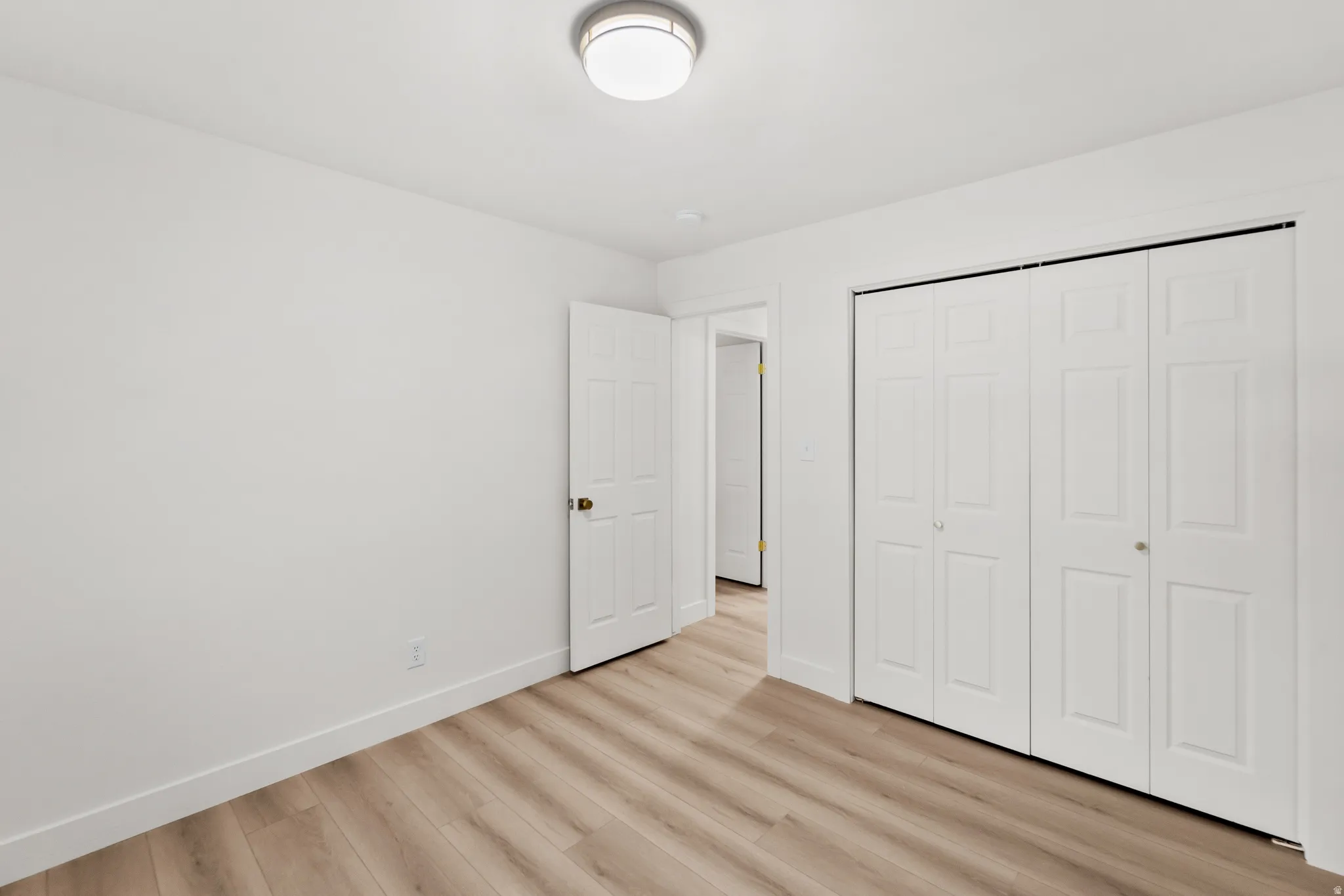 Light-toned wood-finish flooring, white walls, flush mount ceiling light fixture, white interior doors, and bi-fold closet doors