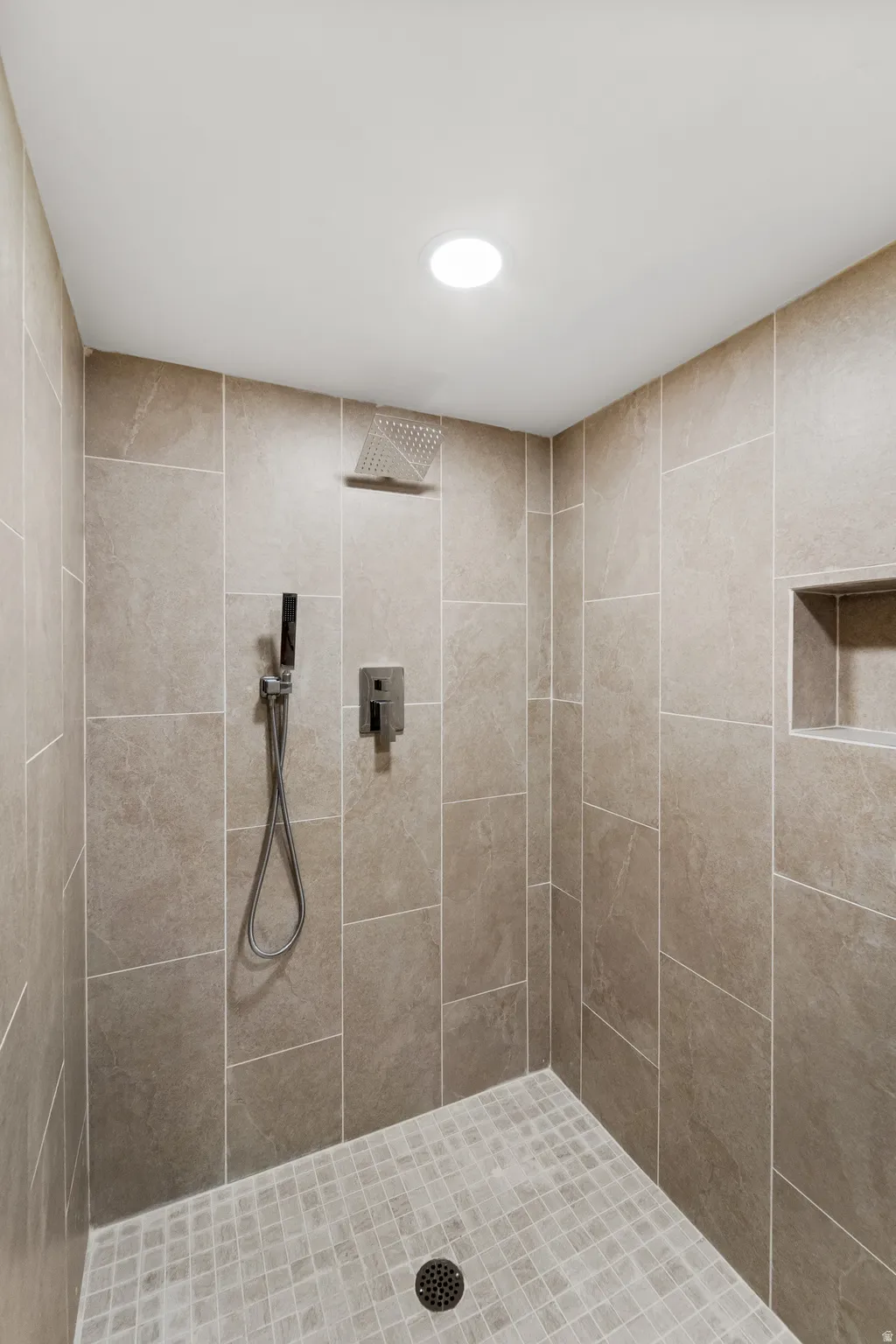Walk-in shower featuring a rain showerhead, handheld shower fixture, recessed niche, and mosaic tile flooring