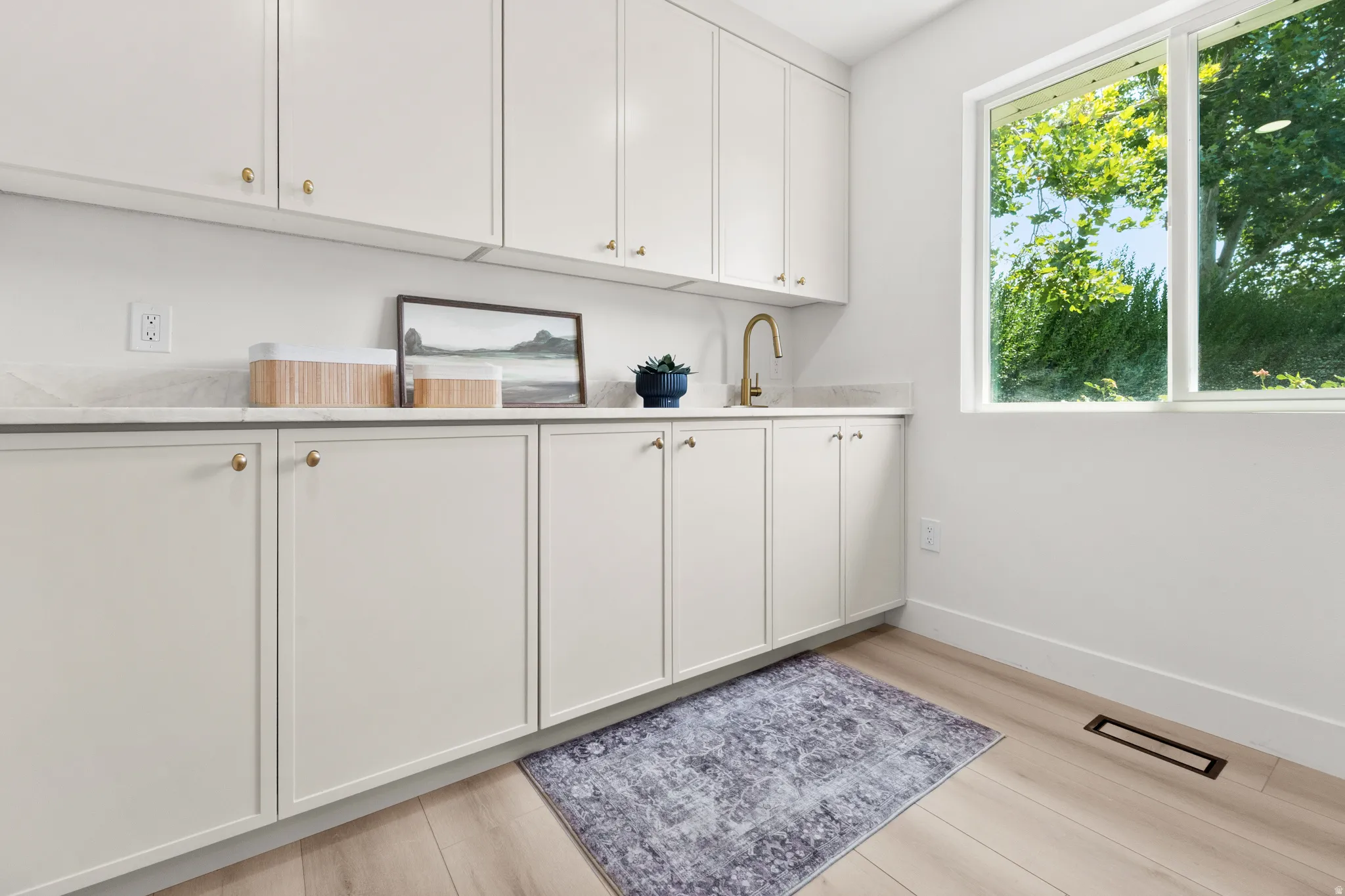 Extensive white cabinetry with gold-toned hardware, light-toned countertop, sink with gold-toned faucet, and wood-finish flooring