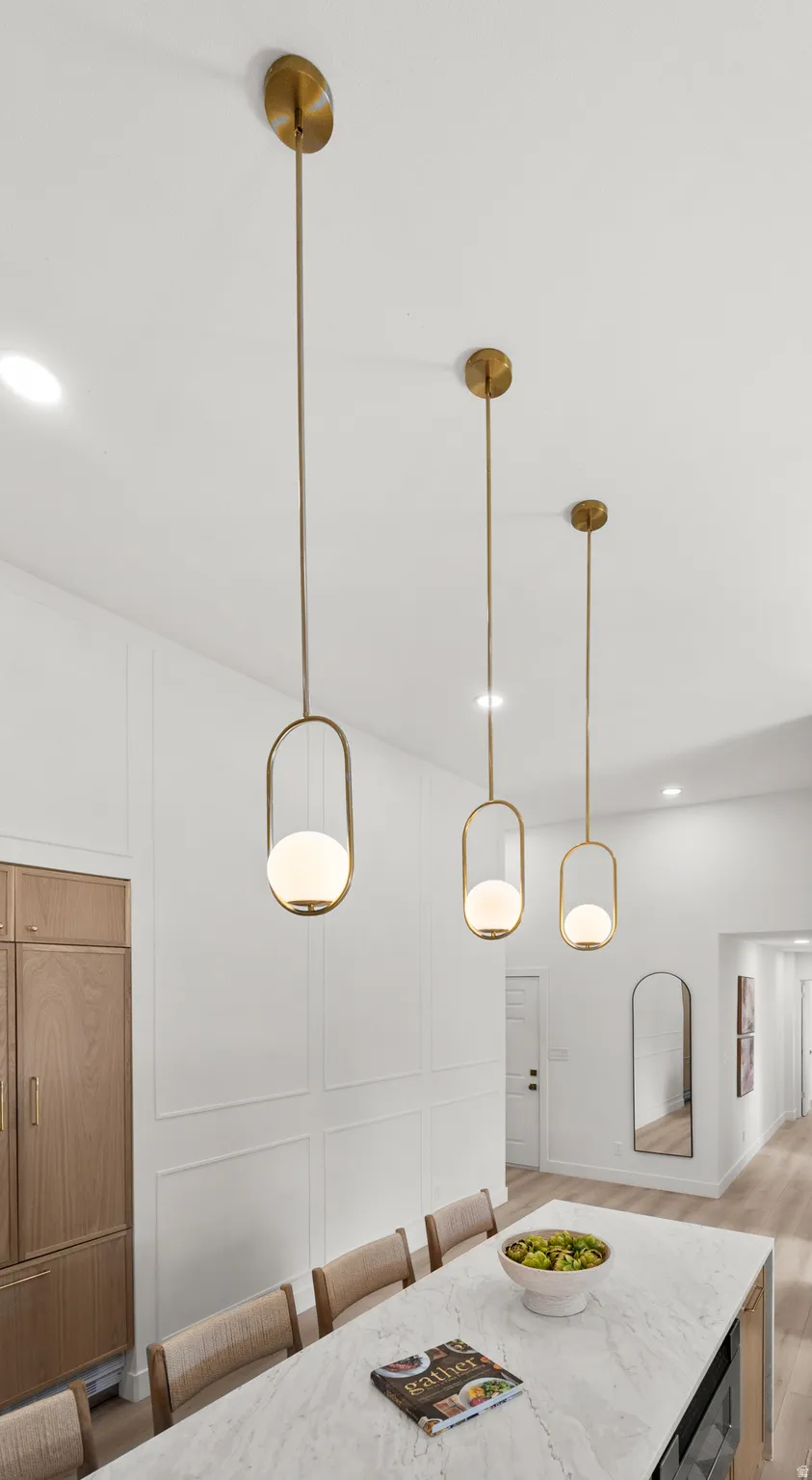 White quartz countertop, three contemporary pendant light fixtures, light wood-finish flooring, built-in panel-ready refrigerator, and decorative wall molding