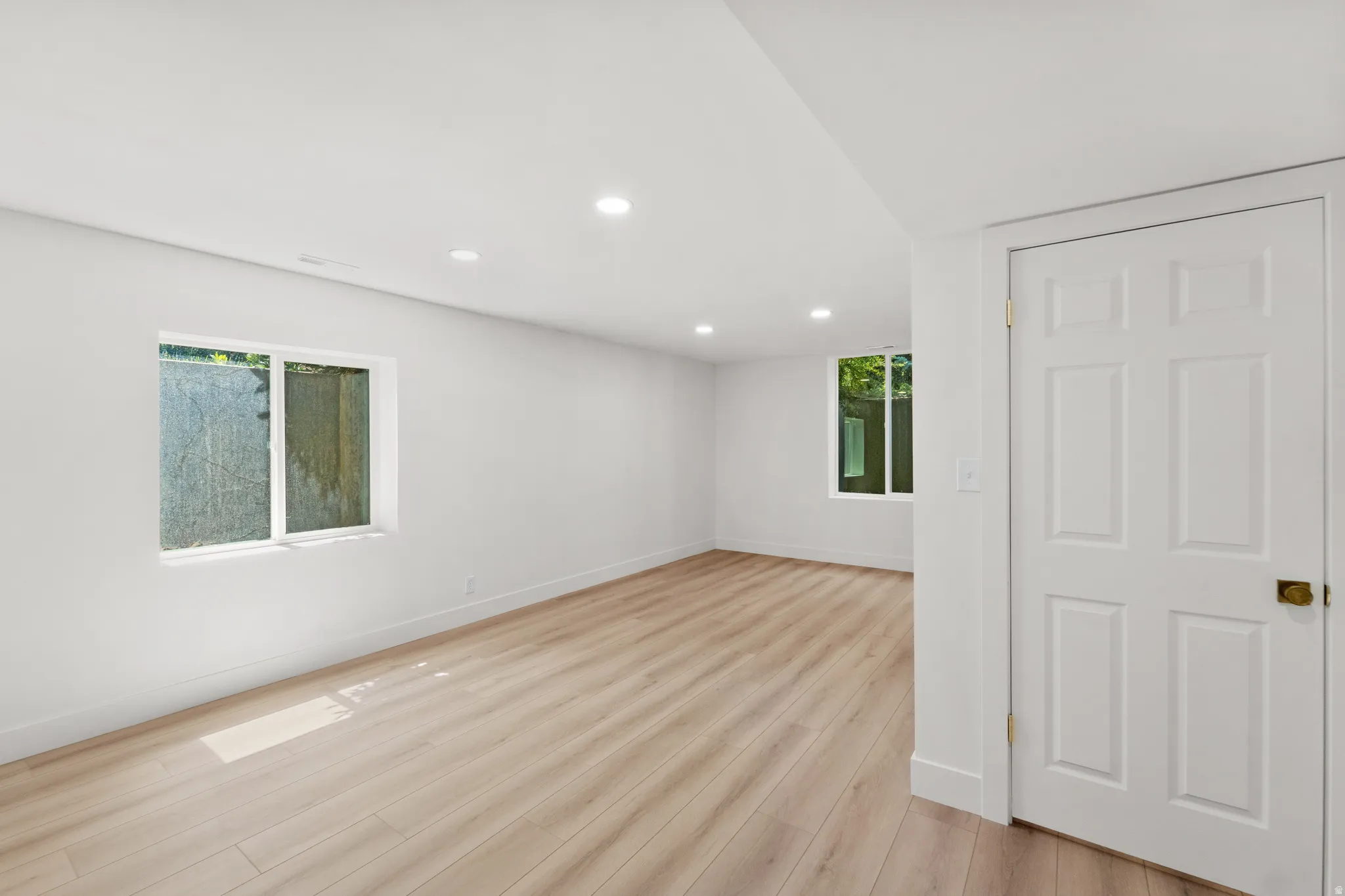 Recessed lighting, light wood-finish flooring, white paneled door, and multiple windows