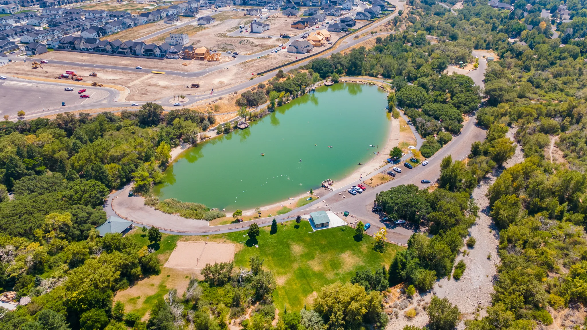 Lakeside setting featuring a sandy beach, surrounding mature trees, and a grassy recreation area