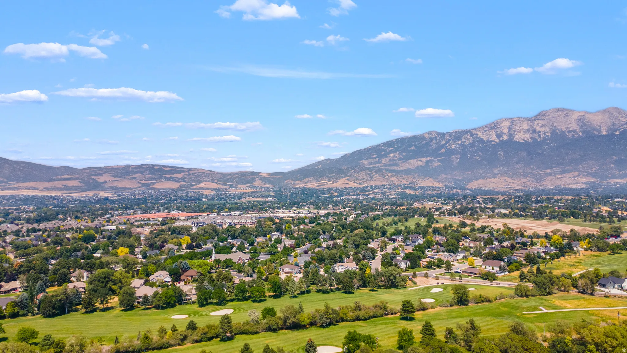 Expansive residential community featuring mature trees, a golf course, and a mountainous backdrop