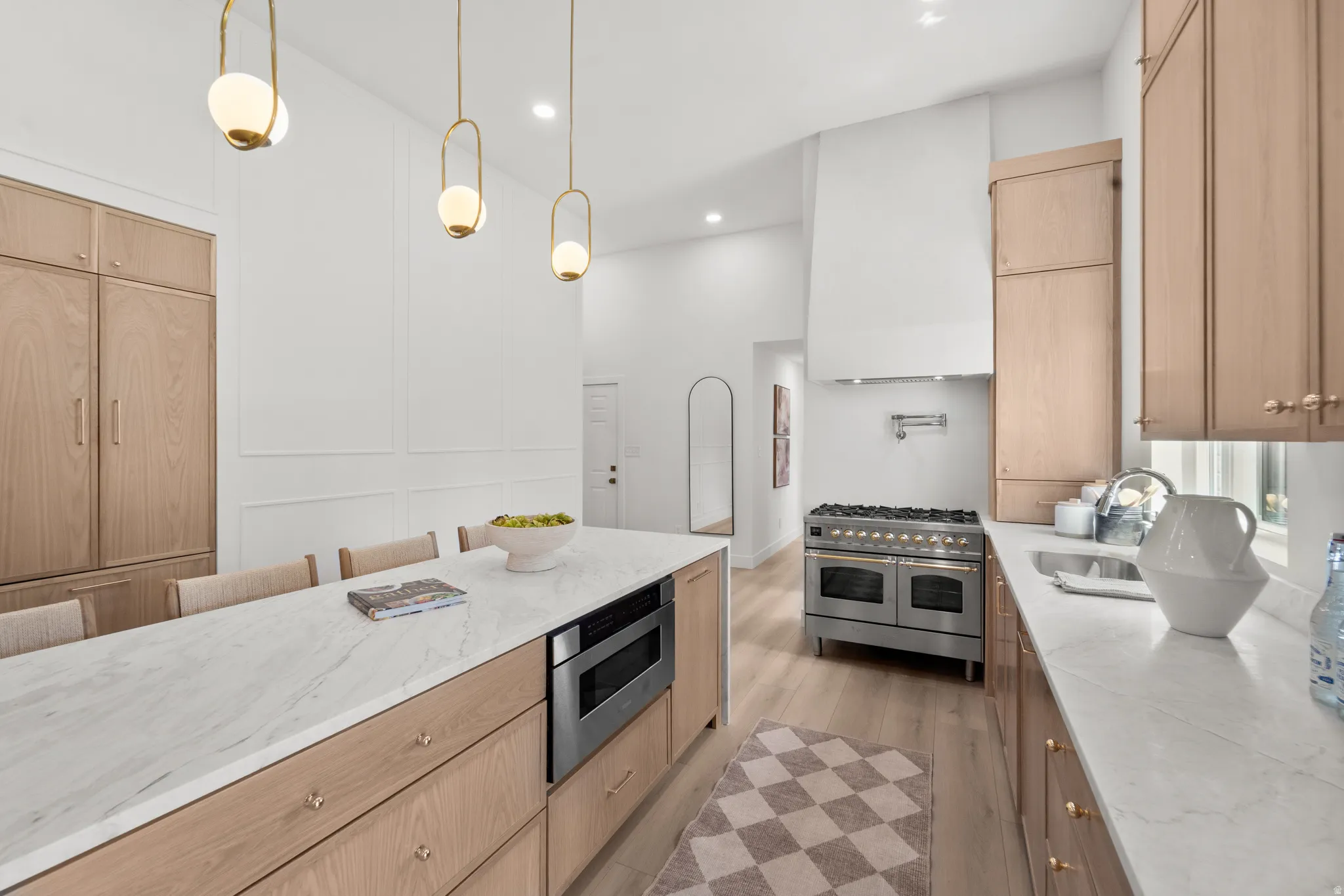 Kitchen featuring light wood-finish cabinetry, a large kitchen island with integrated microwave, stainless steel range with pot filler, and white countertops