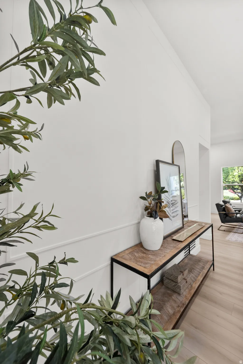 White wall paneling with decorative trim, wood-finish flooring, and a console table featuring a wood top and metal frame