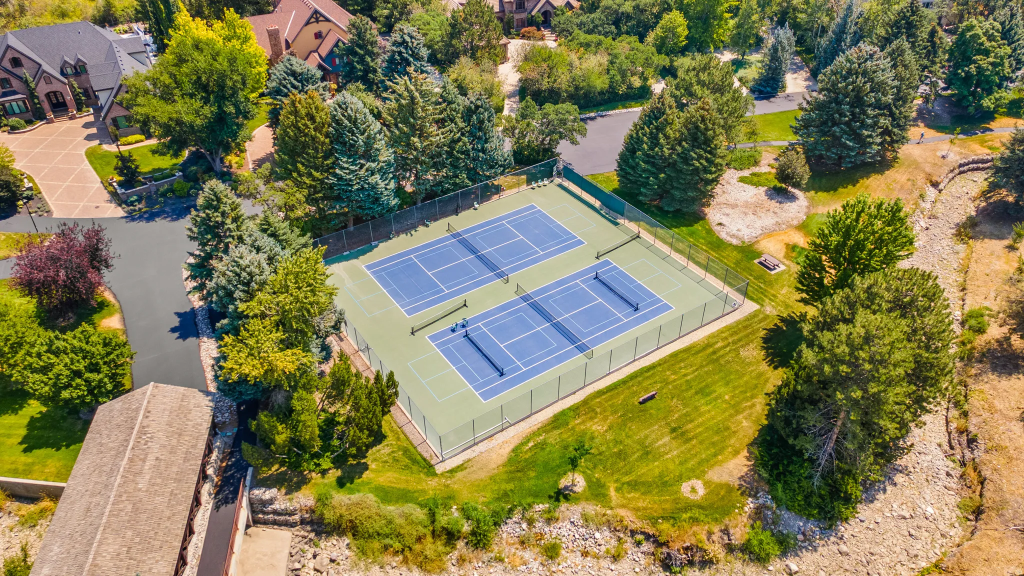 Two full-sized tennis courts with blue playing surfaces and green surrounds