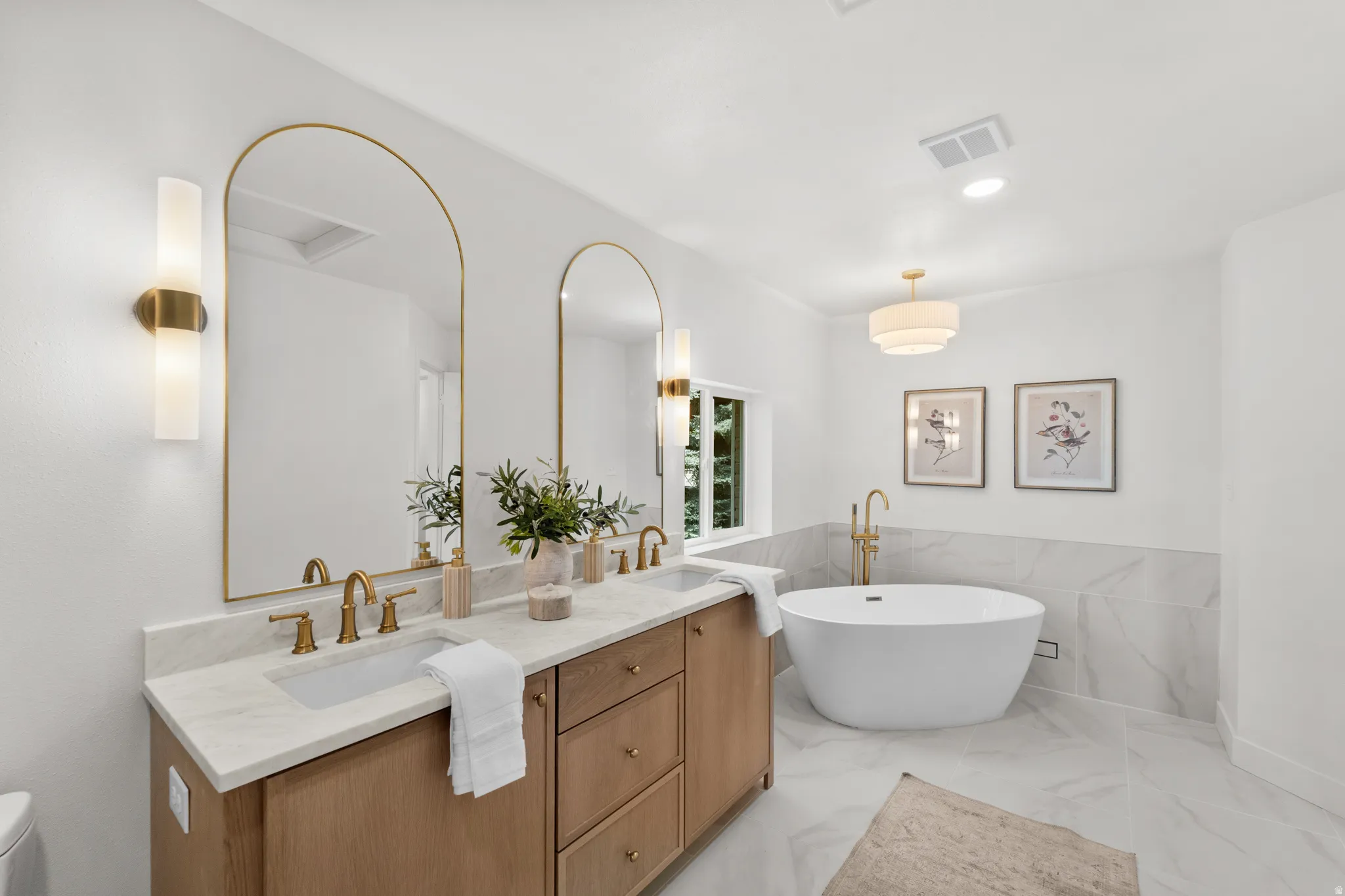 Dual vanity with wood-finish cabinetry, arched mirrors, and brass fixtures