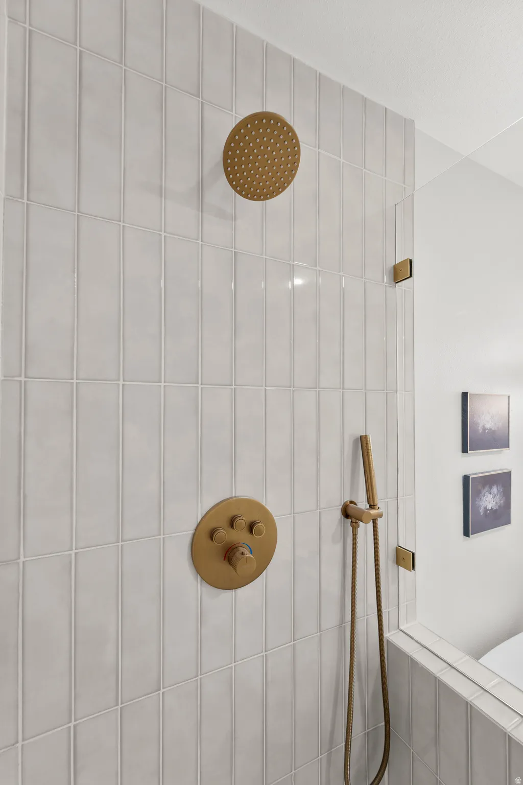 Vertical subway tile shower surround with a rain shower head, handheld shower, and brass fixtures