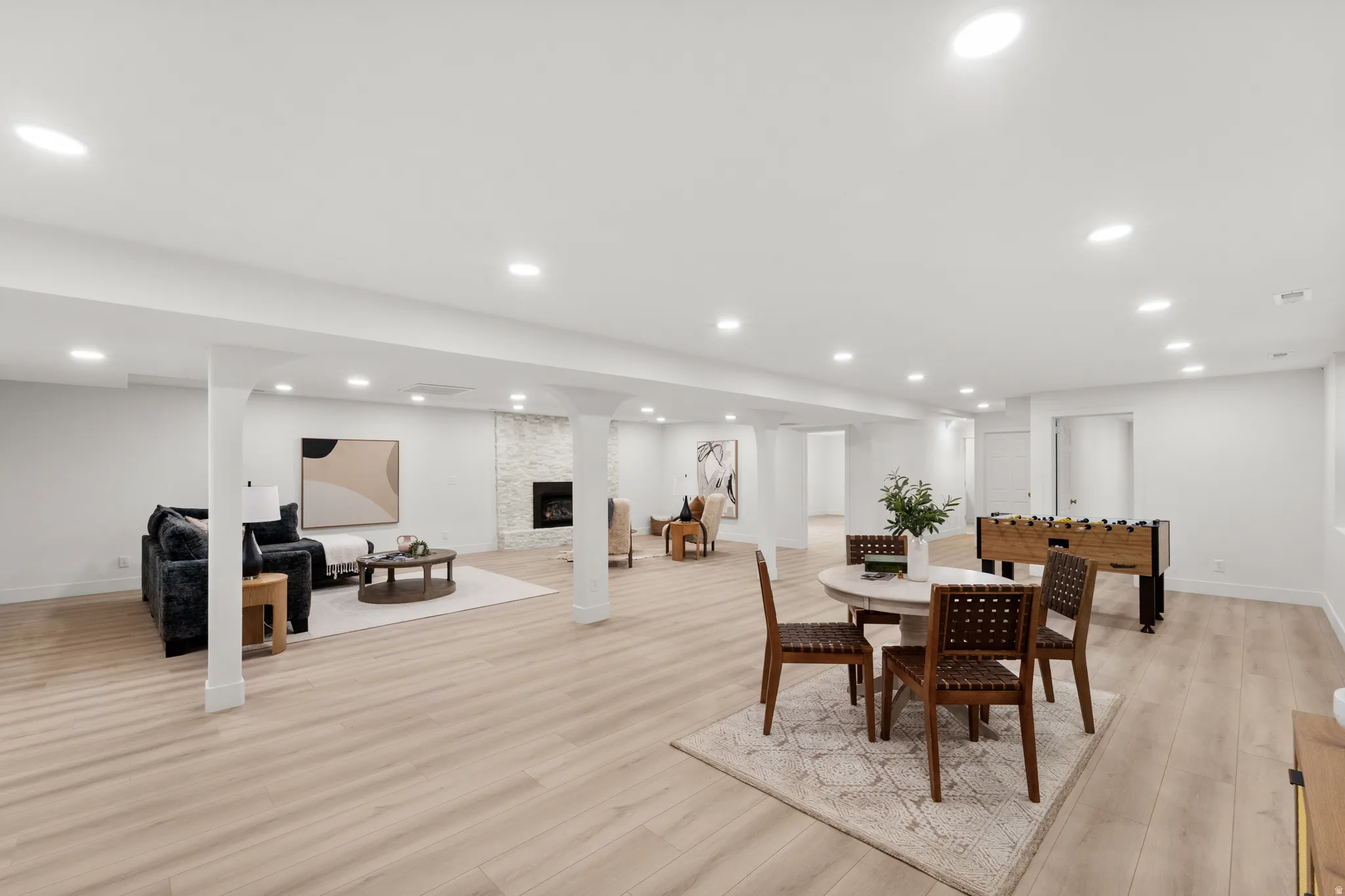 Expansive finished area with light wood-finish flooring, recessed lighting, and a stone-clad fireplace