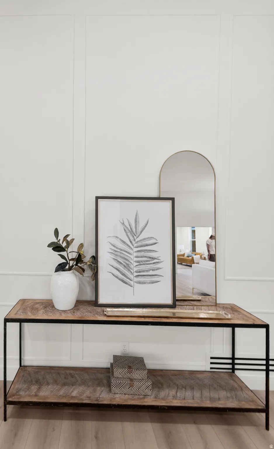 Decorative wall paneling, wood-finish flooring, and a metal-framed console table with two wood-finish display surfaces