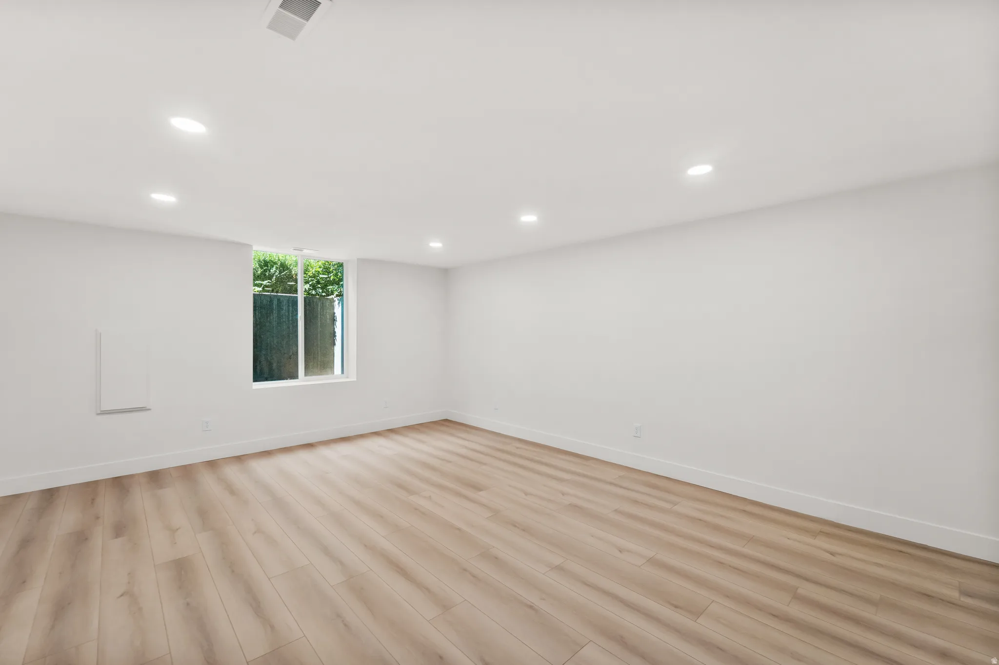 Recessed ceiling lighting, wood-finish flooring, white walls, and a window