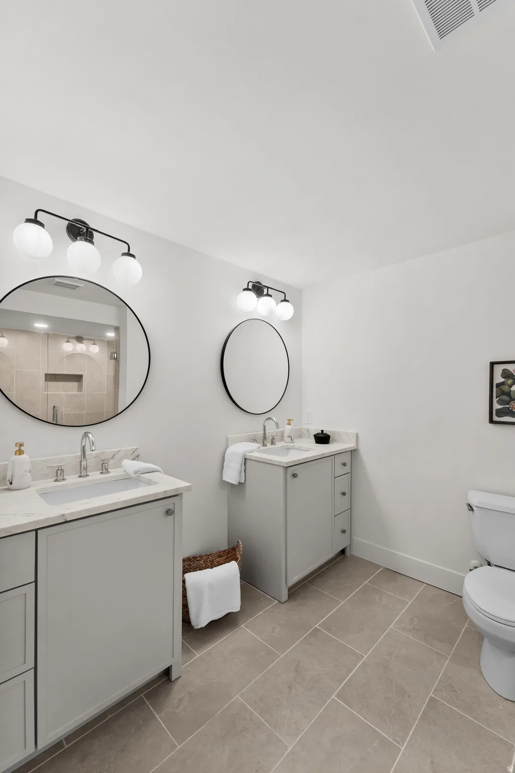 Dual vanities with integrated sinks, light-toned countertops, and black-framed circular mirrors