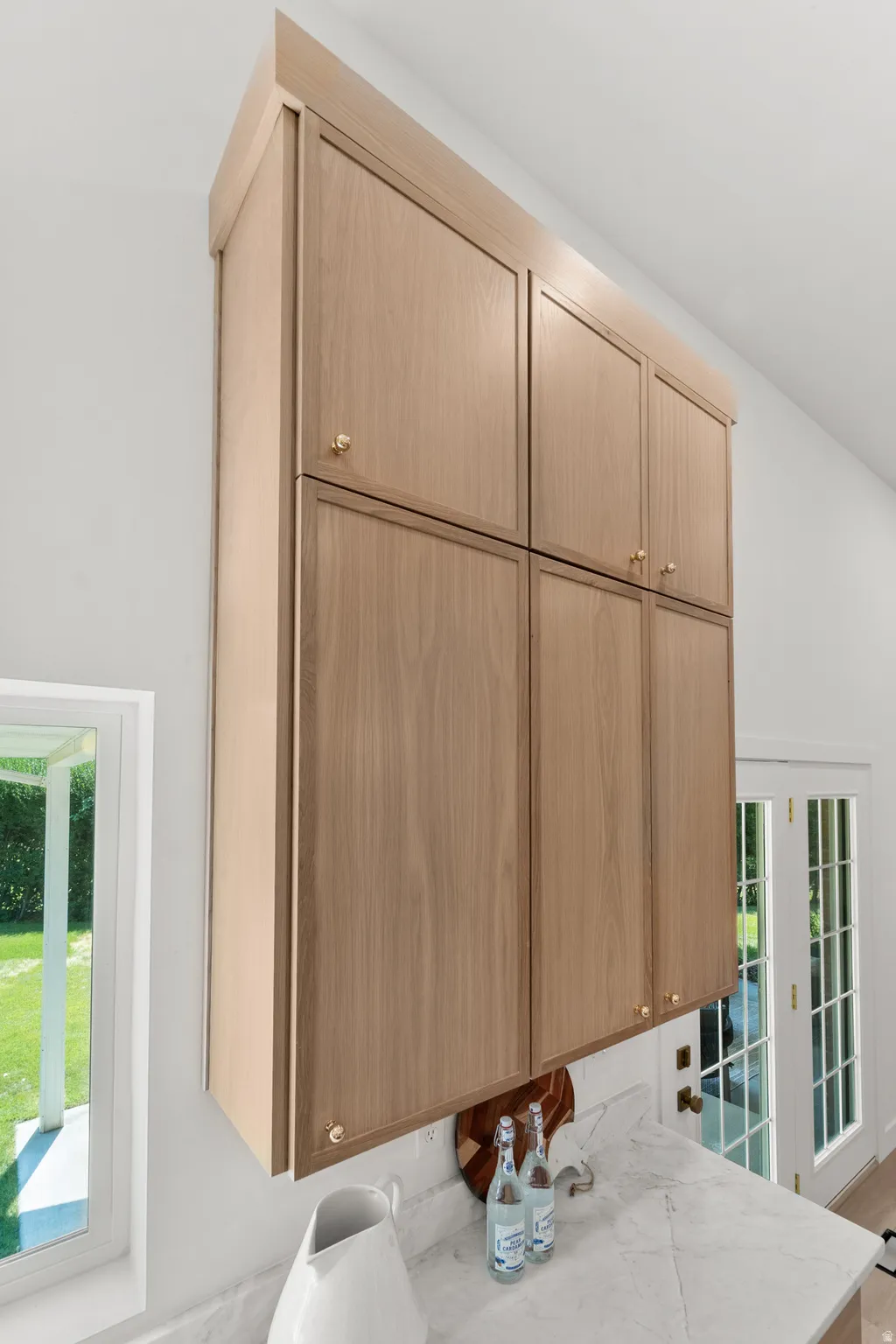 Veneer cabinetry with brass hardware, white marble-finish countertop, and French doors