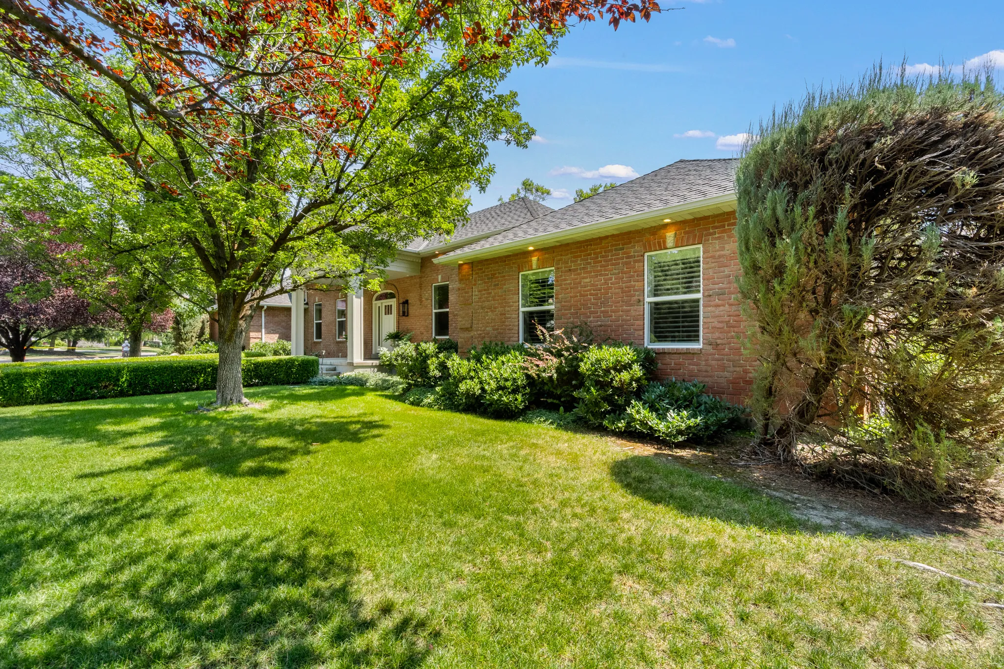 Brick exterior, mature trees, manicured lawn, established landscaping, and a covered portico entry
