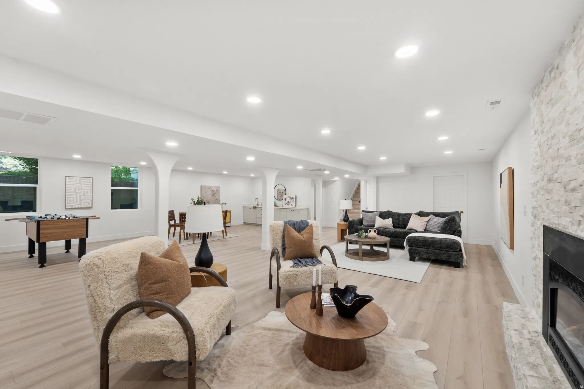 Spacious lower-level living area with recessed lighting, wood-finish flooring, and a stacked stone fireplace