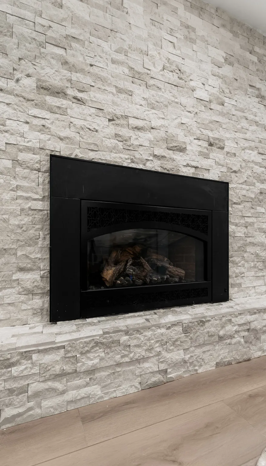 Fireplace with a black insert, stone surround, and wood-finish flooring
