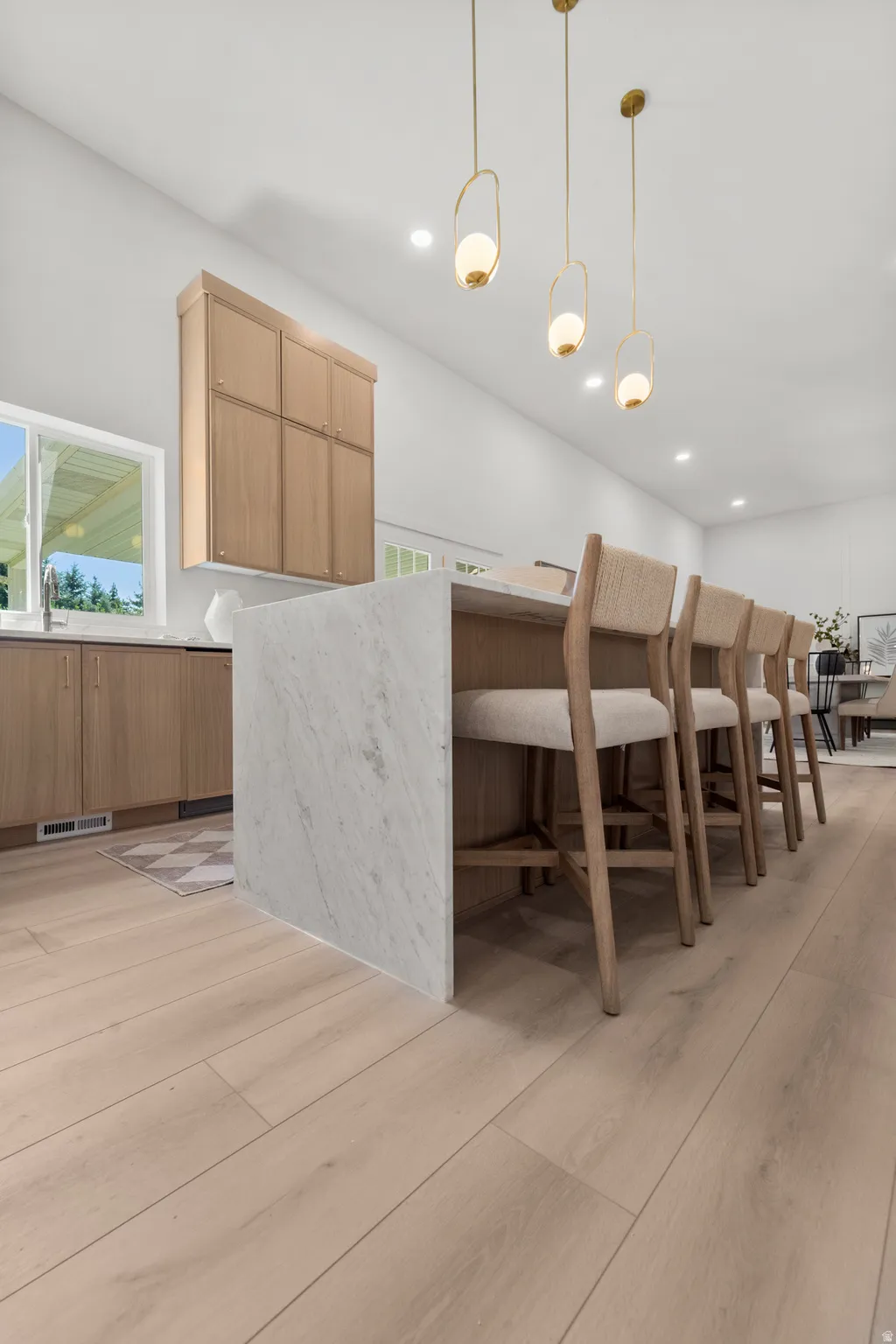 Kitchen featuring a large waterfall island with integrated seating, light wood-finish cabinetry, and recessed lighting
