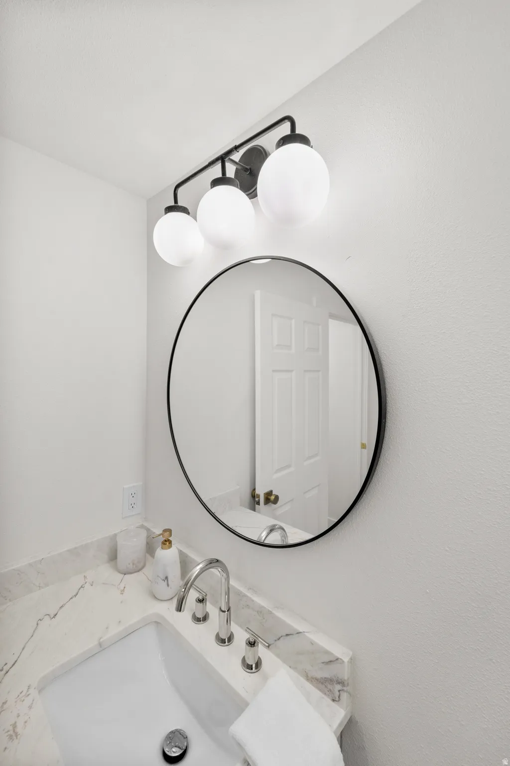 Vanity with integrated sink, polished chrome faucet, round mirror with a black frame, and a three-light vanity fixture