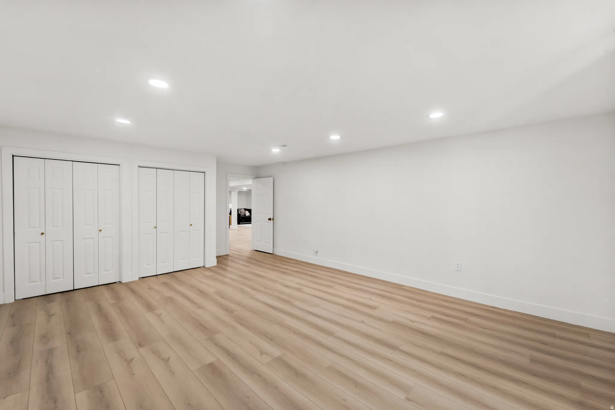 Spacious room featuring light wood-finish flooring, recessed lighting, and multiple bi-fold closet doors