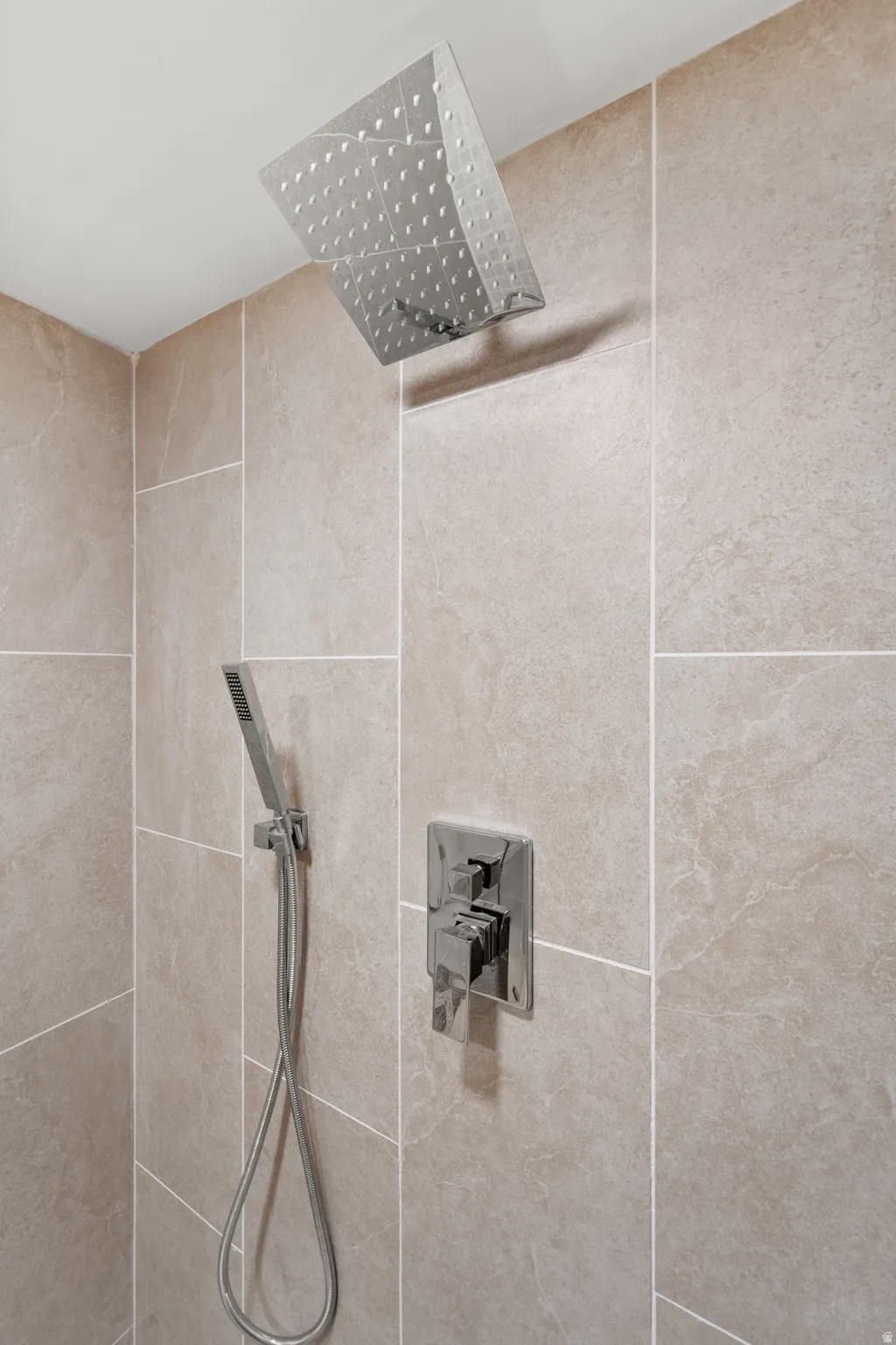 Rainfall showerhead with a handheld spray, integrated shower controls, and large format wall tile