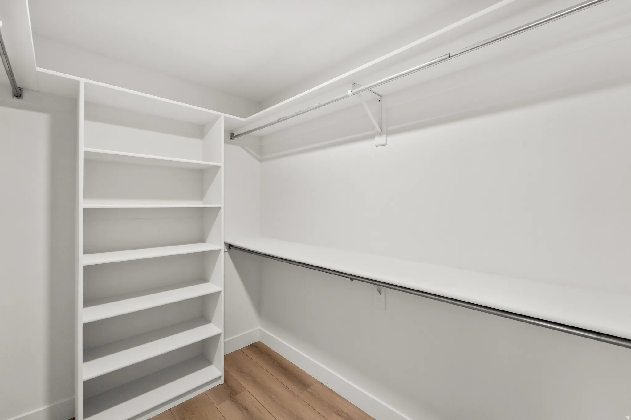 Walk-in closet featuring built-in shelving, white walls, wood-finish flooring, and metal hanging rods