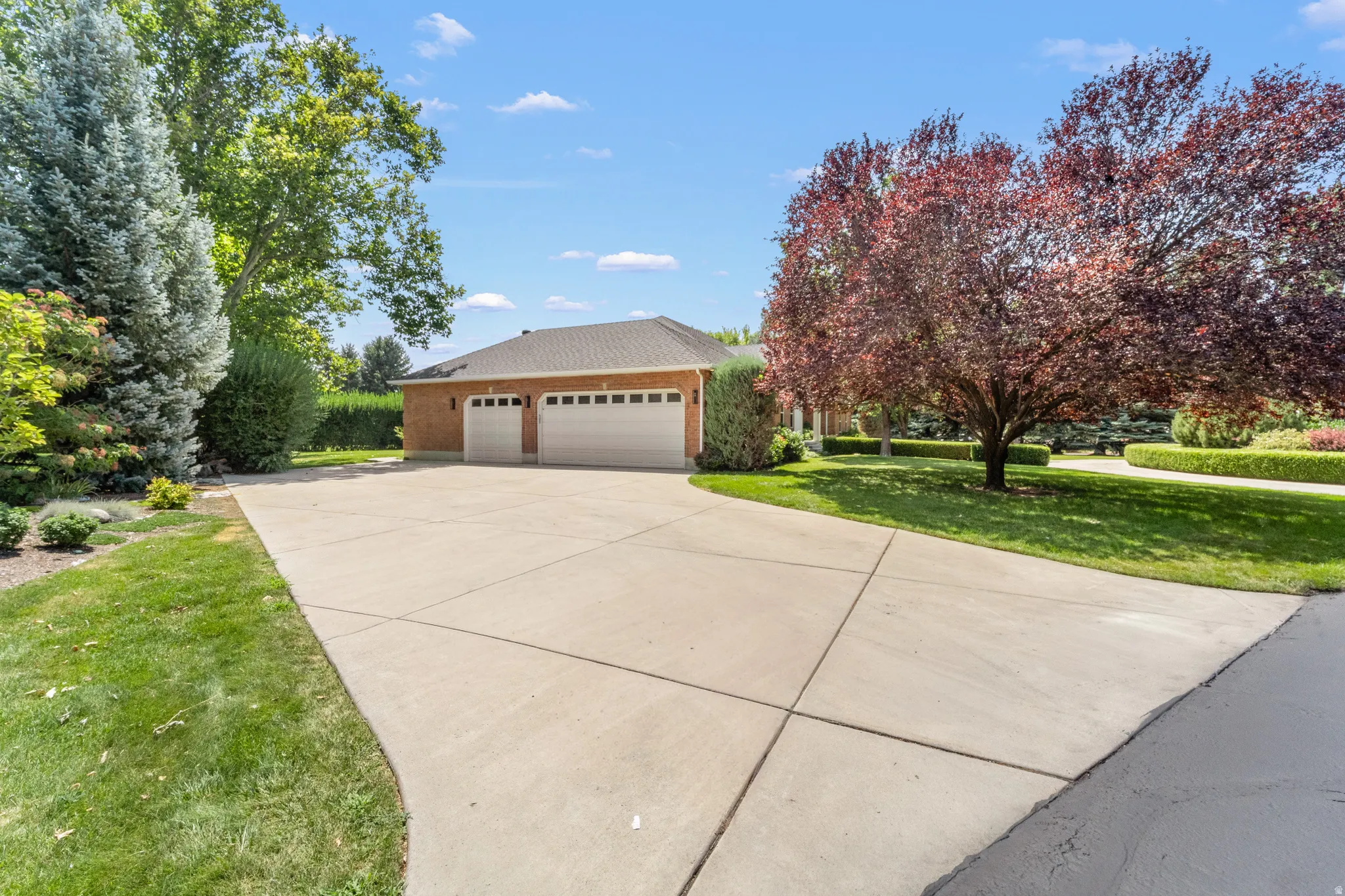 Expansive concrete driveway leading to a two-car garage with brick-finish siding and a shingle roof