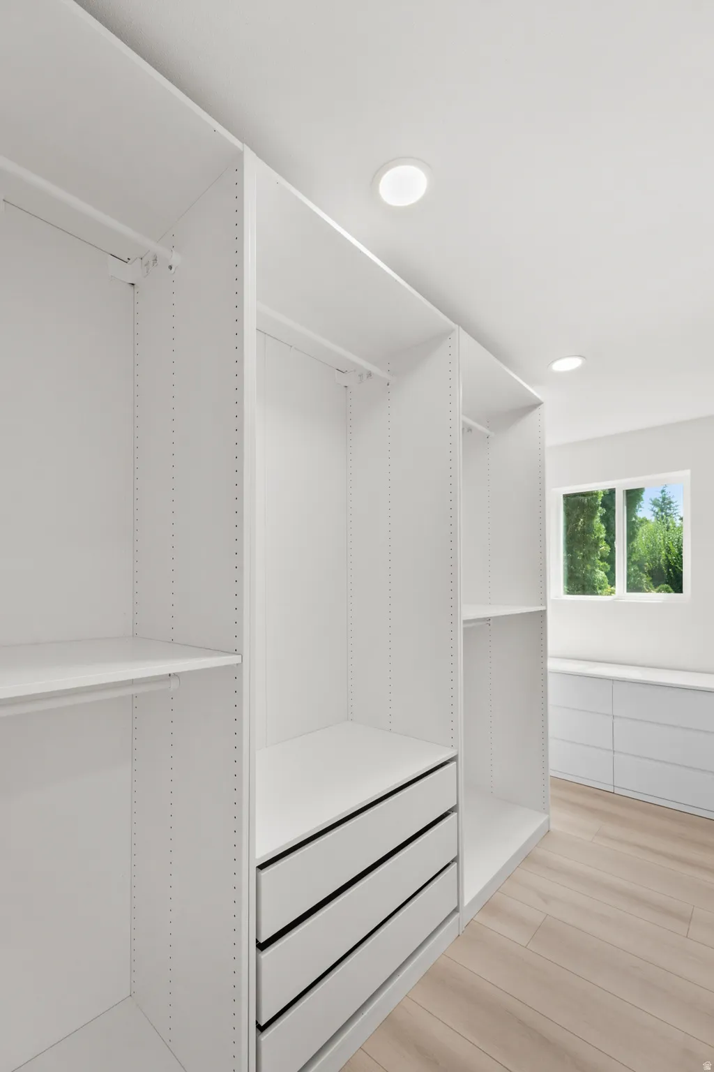 Integrated custom closet system with adjustable shelving, built-in drawers, recessed lighting, and light wood-finish flooring