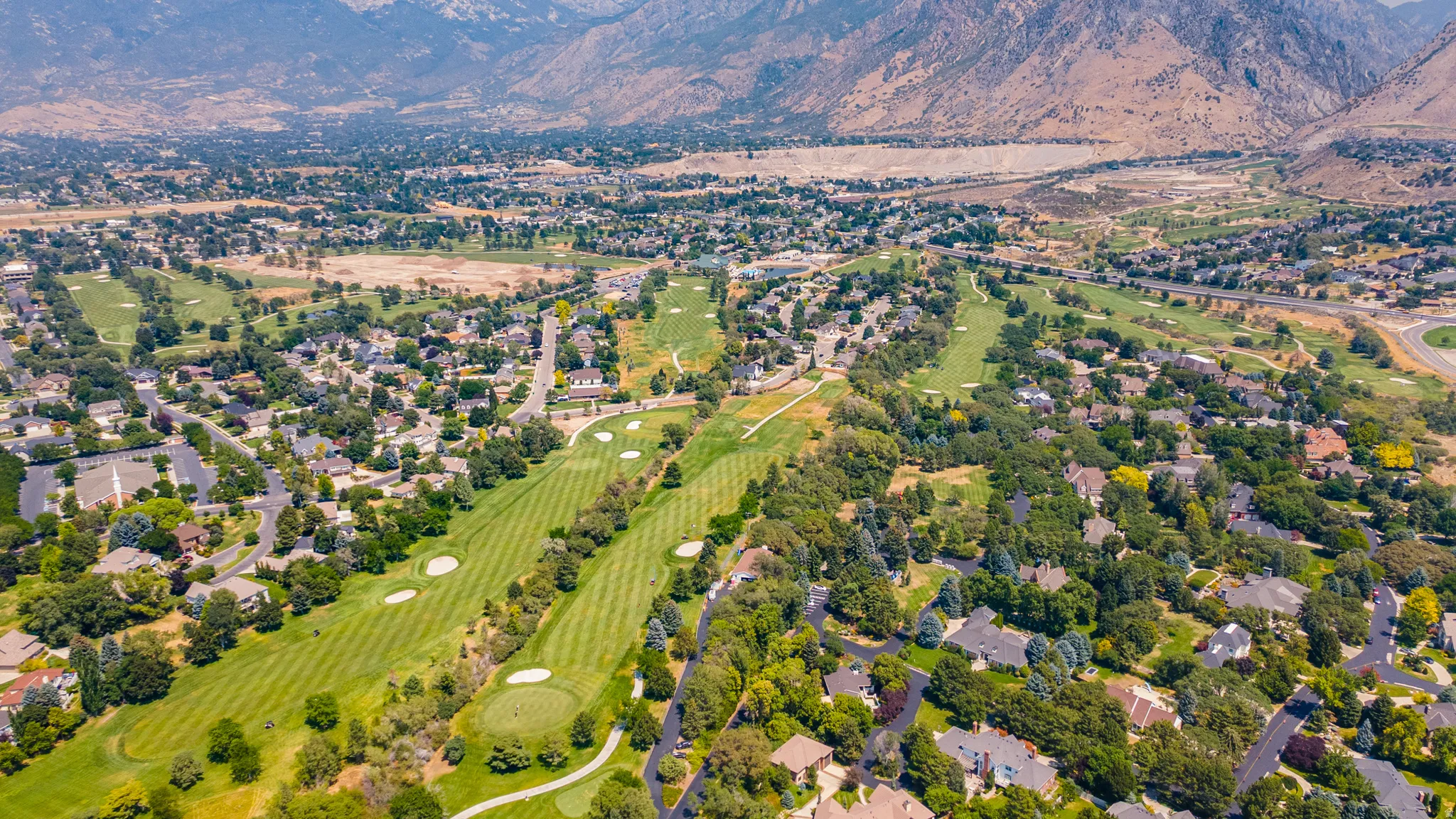 Expansive golf course, mature trees, residential properties, mountain backdrop, paved roadways