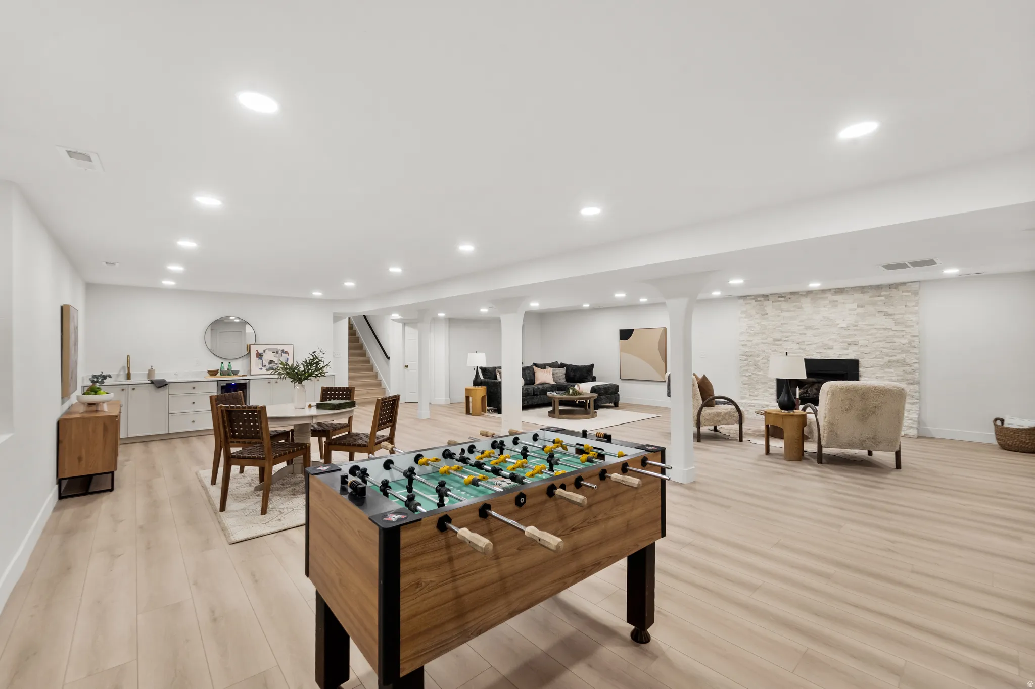 Expansive interior featuring wood-finish flooring, recessed lighting, a stone-clad fireplace, and a built-in wet bar with cabinetry
