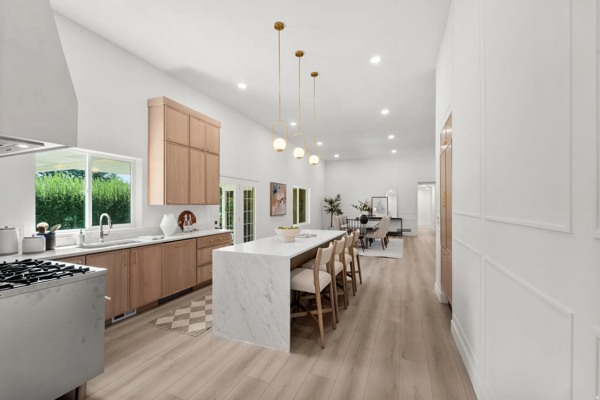 Vaulted ceiling kitchen featuring an oversized island with waterfall edges, light wood-finish cabinetry, stainless steel range, and light wood-finish flooring