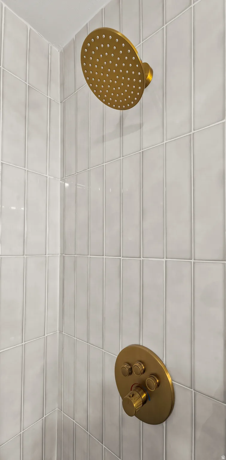 Vertical-set subway tile surround with a matte gold rain shower head and matching control panel