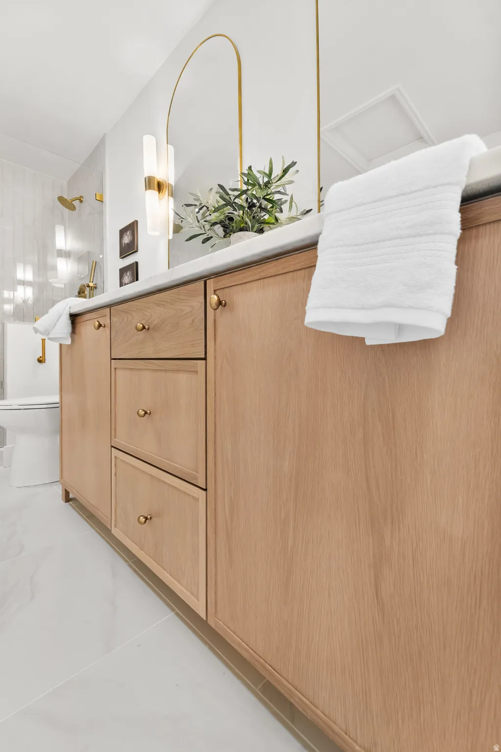 Custom wood-finish vanity with brass hardware, a light-toned countertop, and a sleek arched mirror
