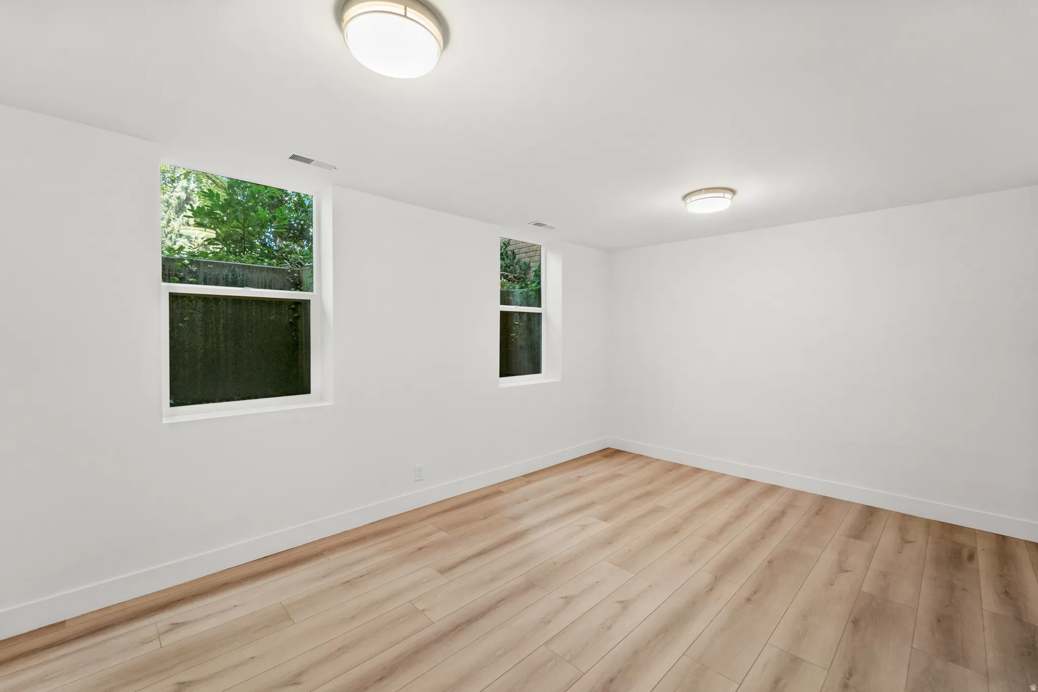 Bright interior space featuring wood-finish flooring, white walls, and dual flush-mount ceiling lights