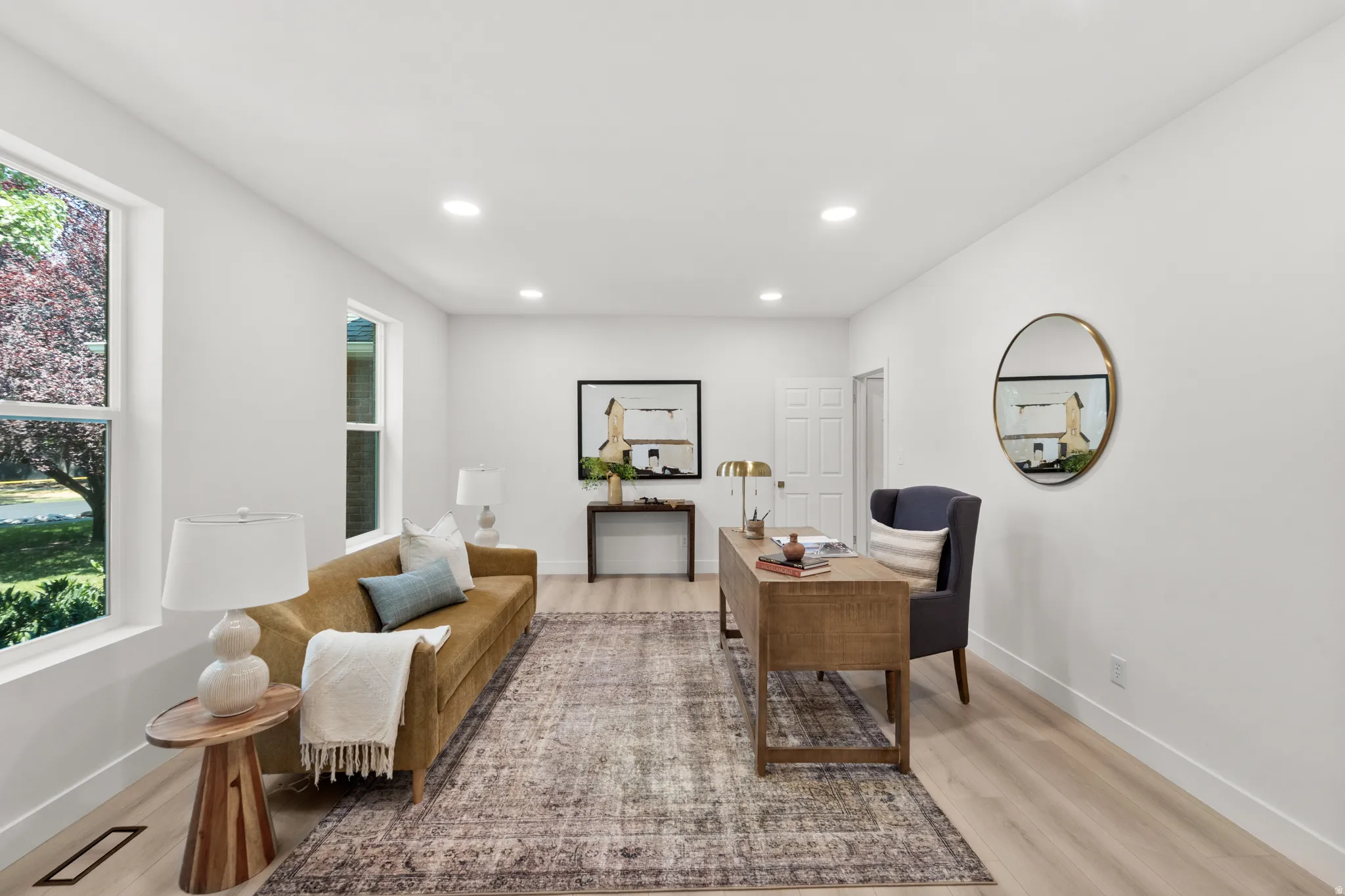 Recessed lighting, light wood-finish flooring, multiple windows, white walls, and a white paneled door