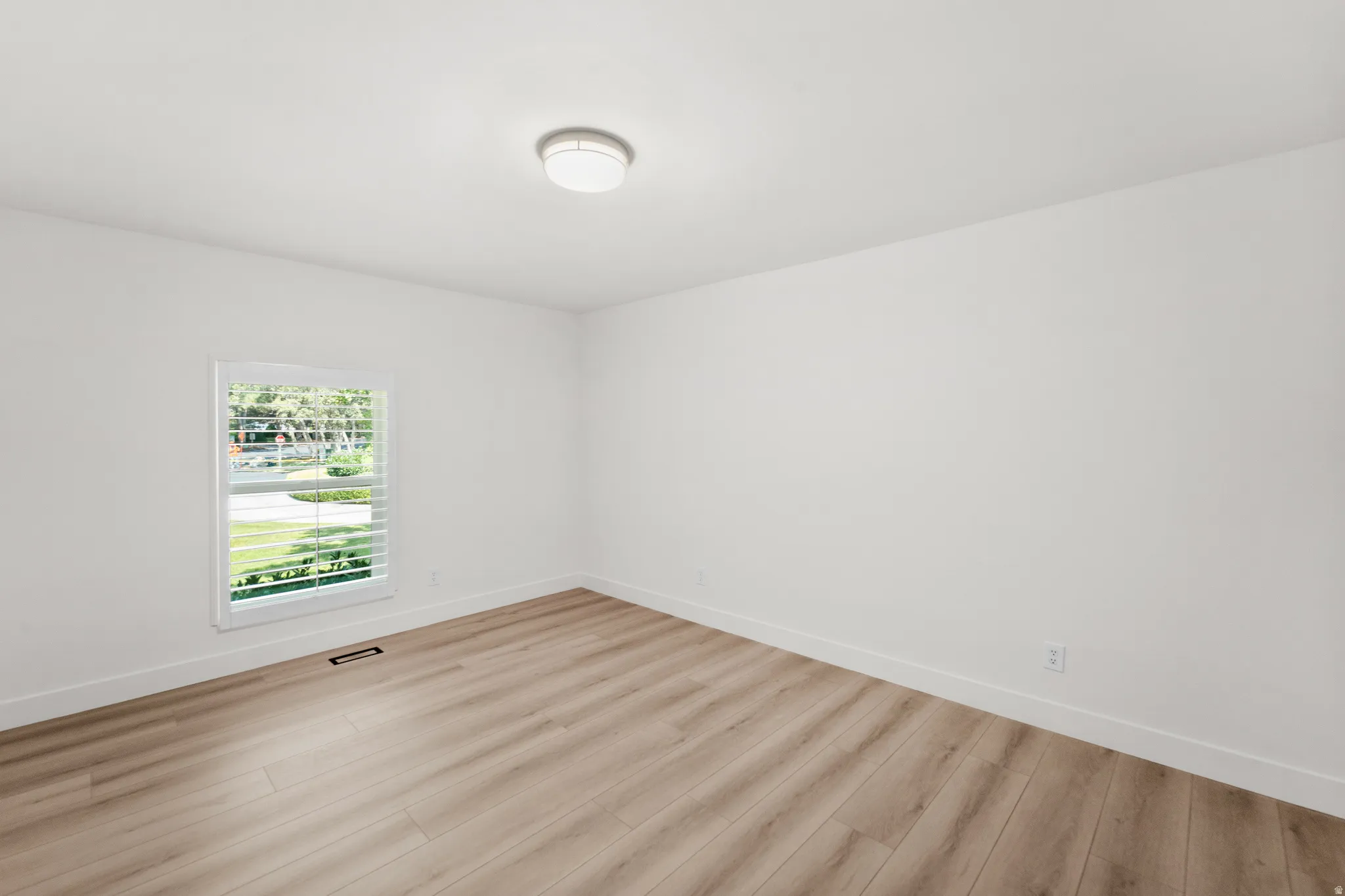 Recessed lighting, light wood-finish flooring, white walls, and a window with plantation shutters