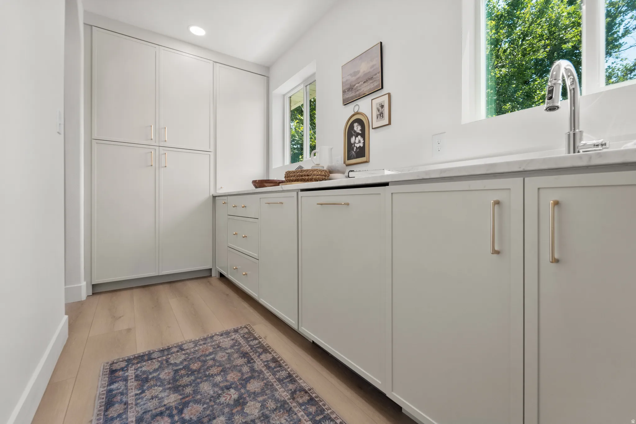 Integrated cabinetry with brushed gold hardware, undermount sink with chrome faucet, light wood-finish flooring, and natural light from a window