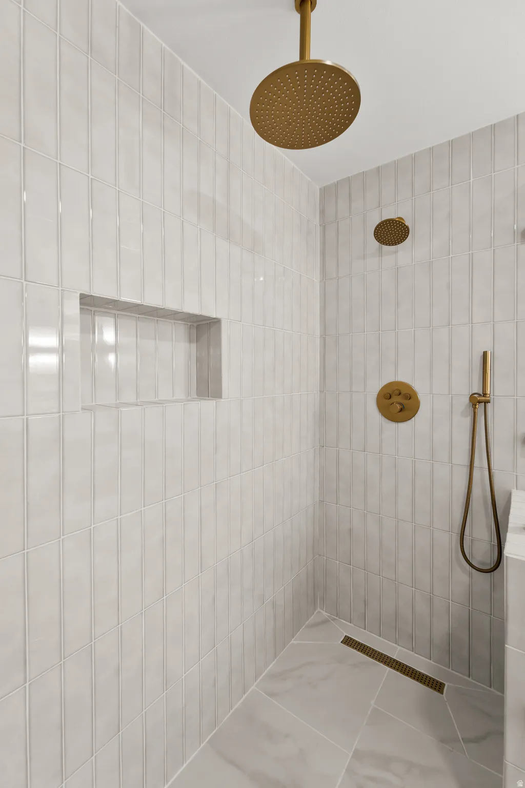 Shower featuring ceiling-mounted rain showerhead, wall-mounted showerhead, hand shower, and linear drain, all in a brass finish