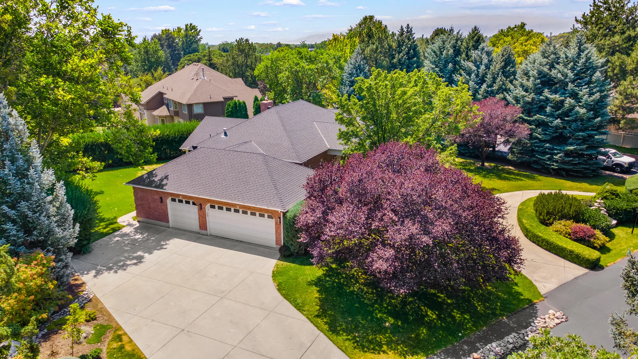 Brick exterior, three-car garage, concrete driveway, mature landscaping, and established trees