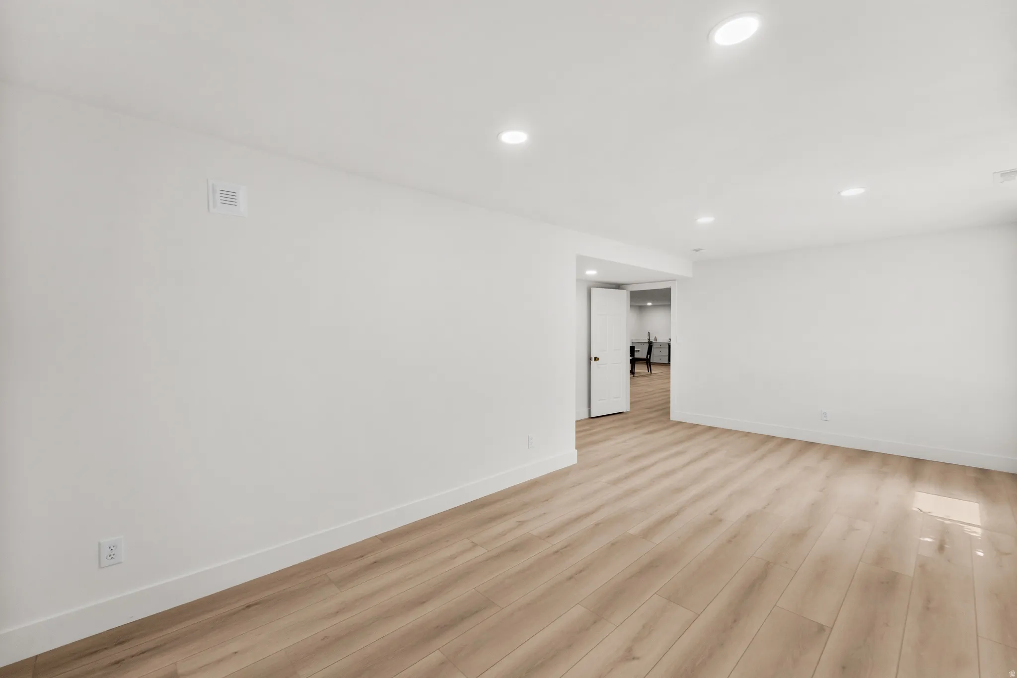 Recessed ceiling lighting, light wood-finish flooring, white walls, white trim, and a white interior door with dark hardware