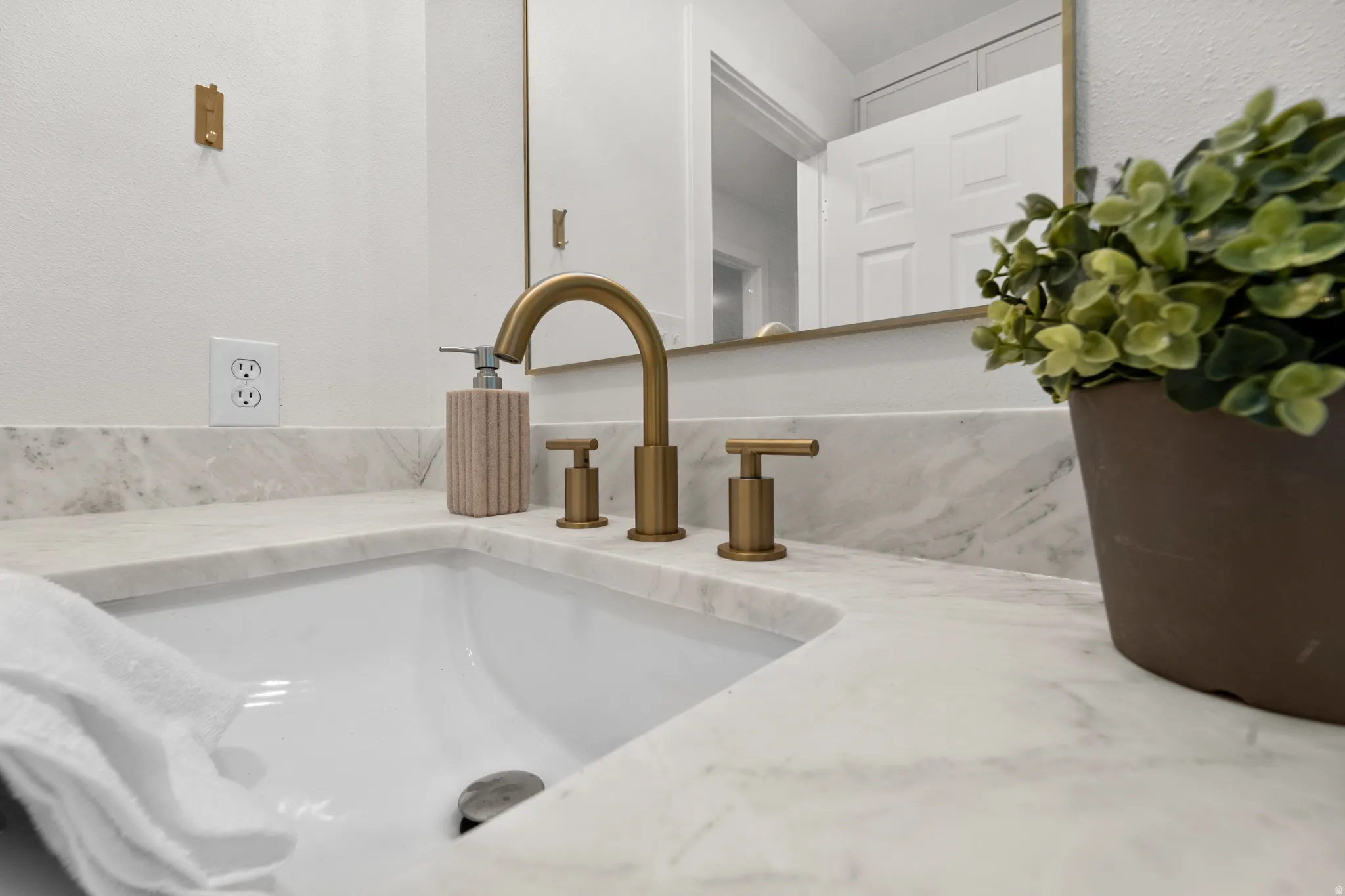 Undermount sink with a light-toned countertop, a three-piece brass-finish faucet, and a brass-finish framed mirror
