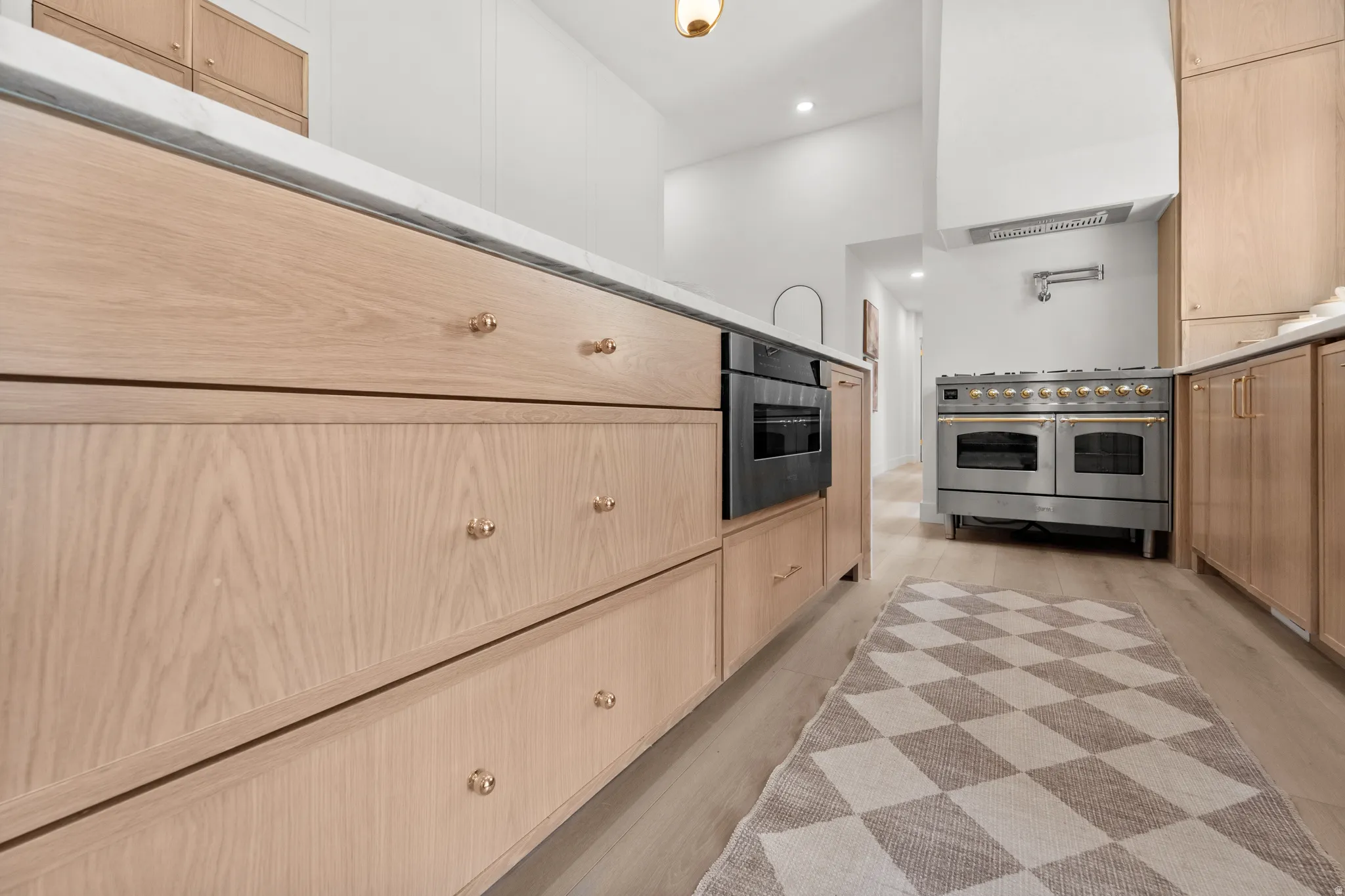 Custom cabinetry with brass hardware, integrated wall oven, white countertop, professional-grade range, and wood-finish flooring