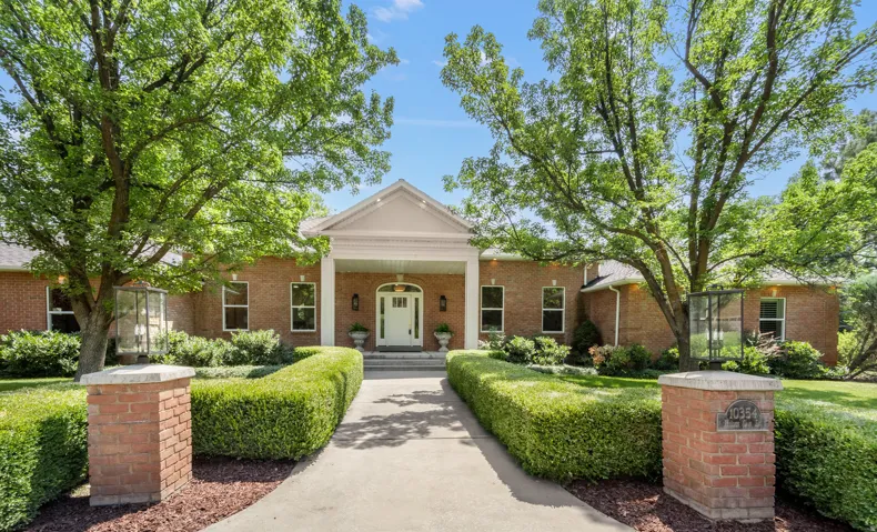 Brick Colonial estate anchored by a gabled portico and flanked by mature shade trees