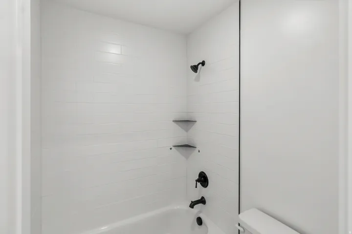 White subway tile shower surround with integrated corner shelves, matte black shower fixtures, and a white bathtub